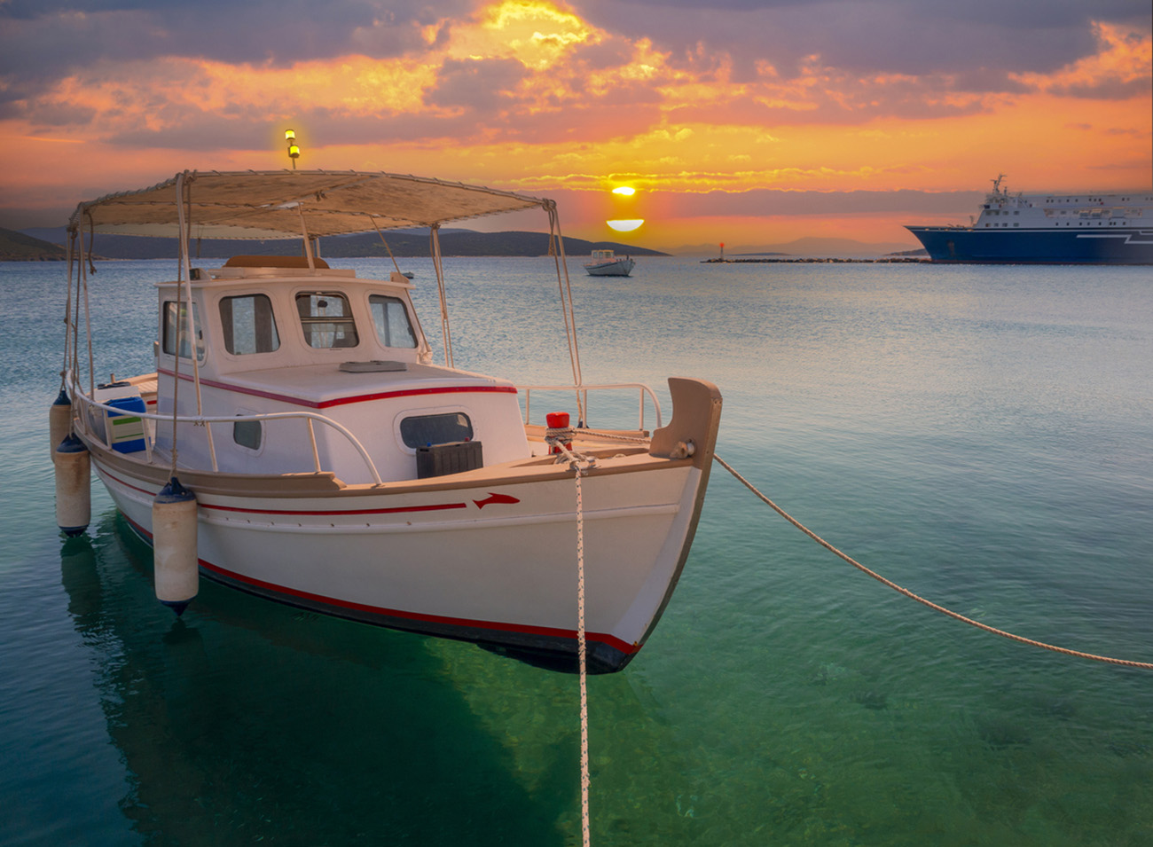 White fishing boat with an awning in port of Greek resort town Marmari at sunset on island Evia in Greece