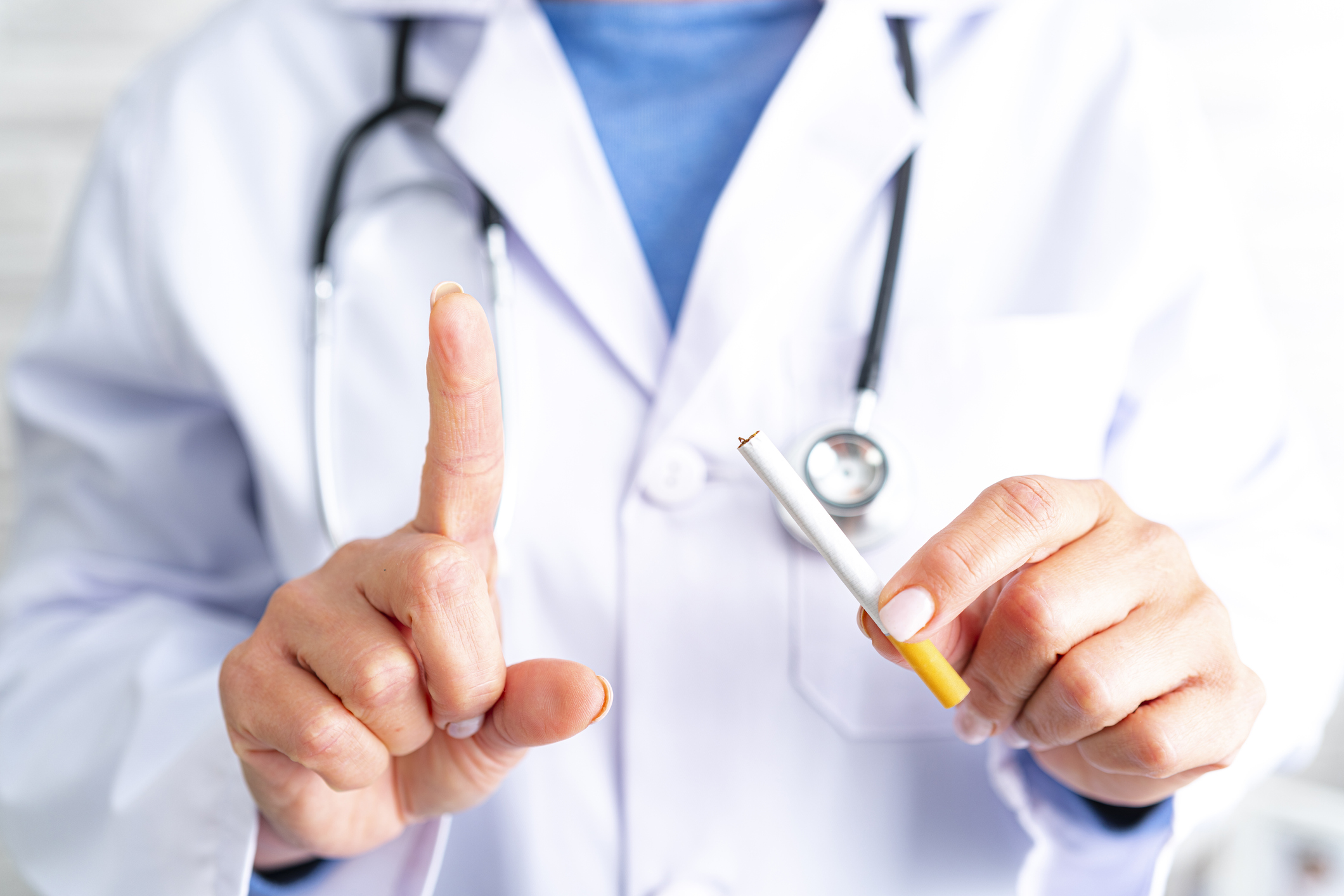 Close up view of female Medical Doctor hands holding cigarette and raising index finger. Smoking tobacco is a risk for health. Predominant color is white. Selective focus on foreground. High resolution 42Mp studio digital capture taken with Sony A7rII and Sony FE 90mm f2.8 macro G OSS lens