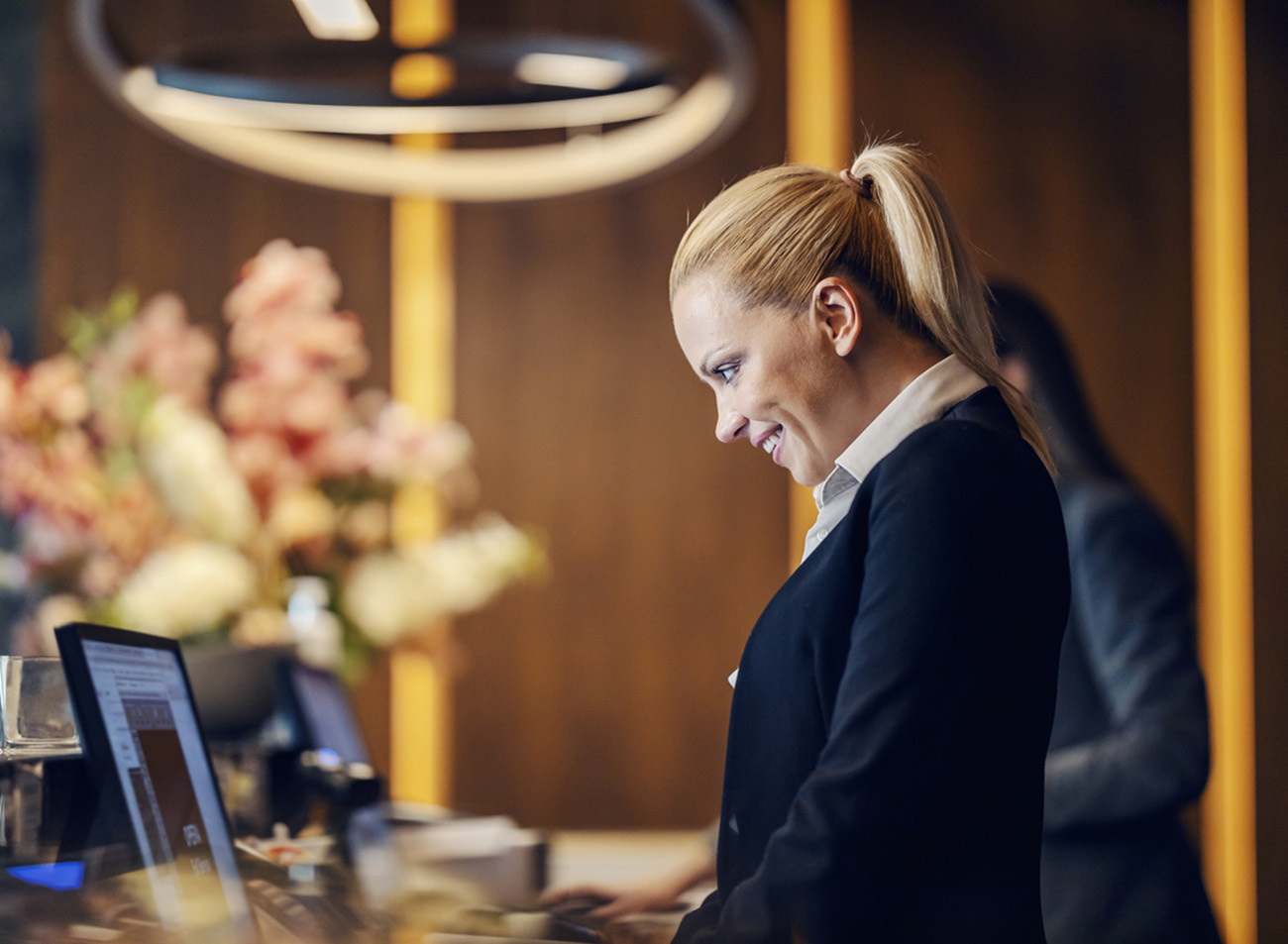 A happy receptionist is making an online reservation on computer while standing at reception.