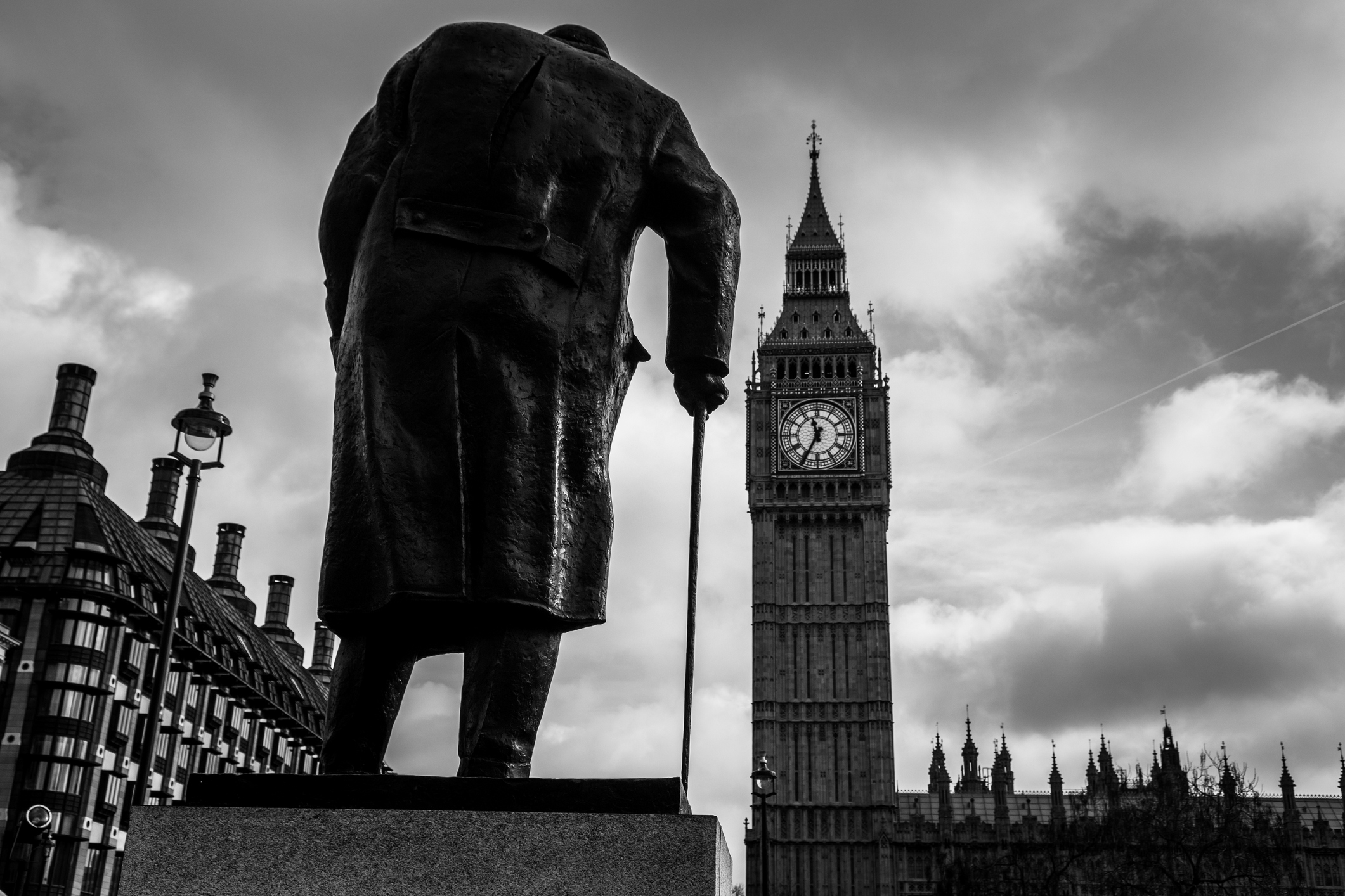London, UK - February 16, 2017: rear view of a statue of Winston Churchill, the famous British prime minister, overlooking the iconic Big Ben clock tower and houses of parliament. The sky is moody with patches of blue. Horizontal black and white image with copy space.