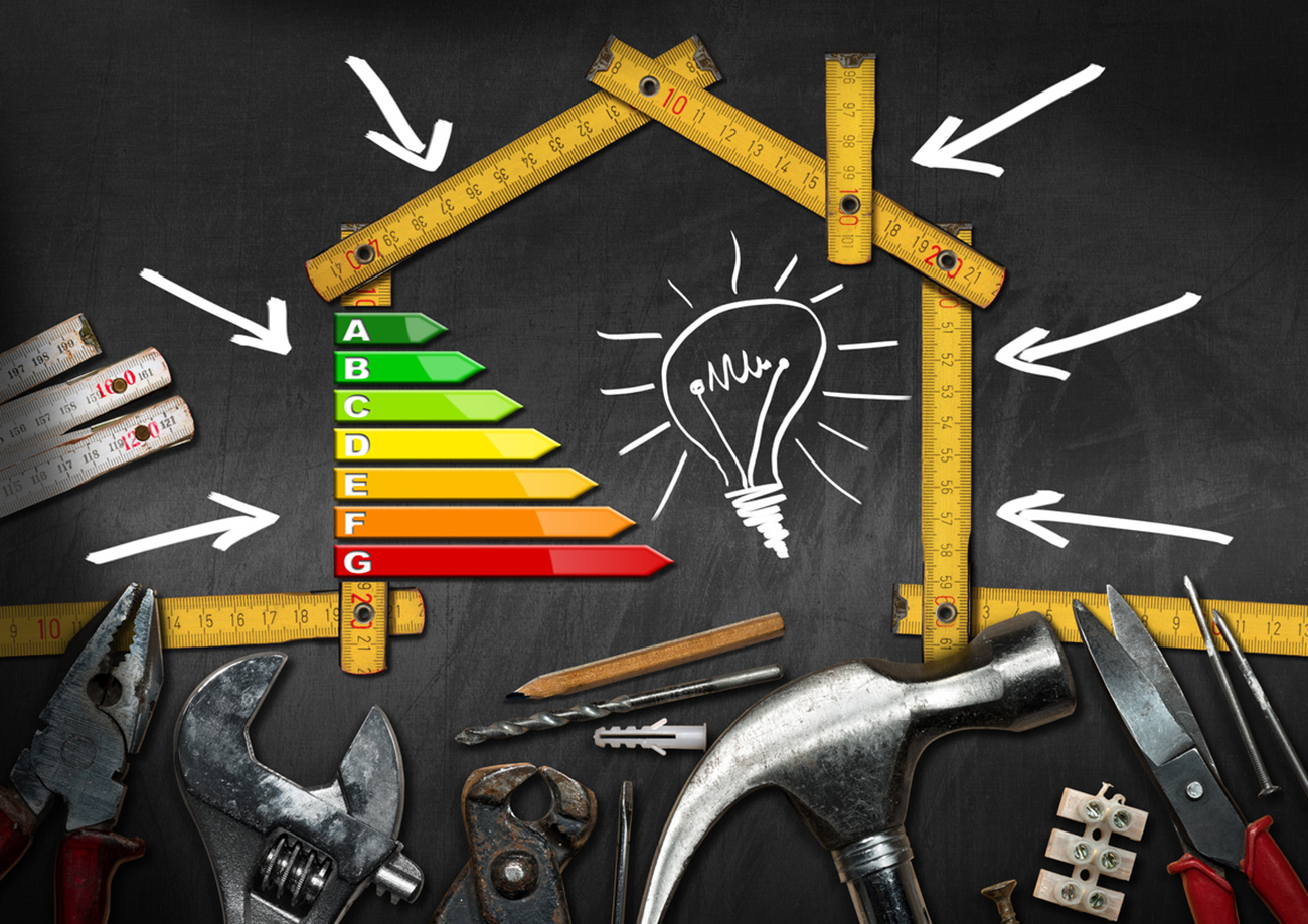 Home improvement concept - Wooden ruler in the shape of a house with energy efficiency rating on a blackboard with work tools and a light bulb