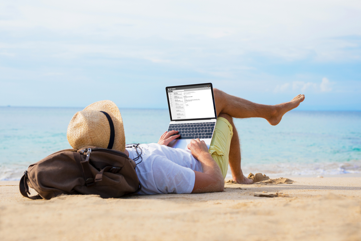 Unrecognizable male reading email on laptop while relaxing on beach