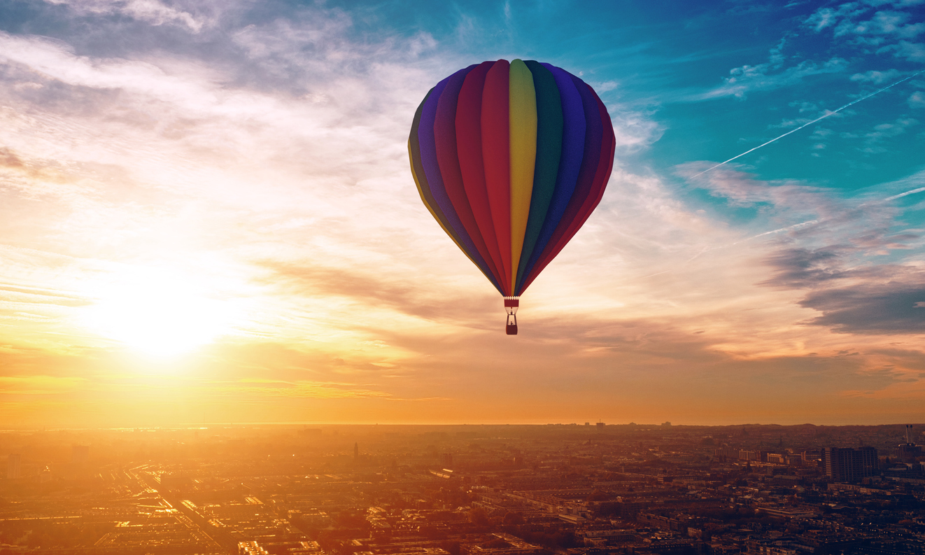 Hot air ballon with different colors travels across the sky. A city is below and rooftops are visible. 
Note: The hot air ballon is made in a 3D program. Property release attached.