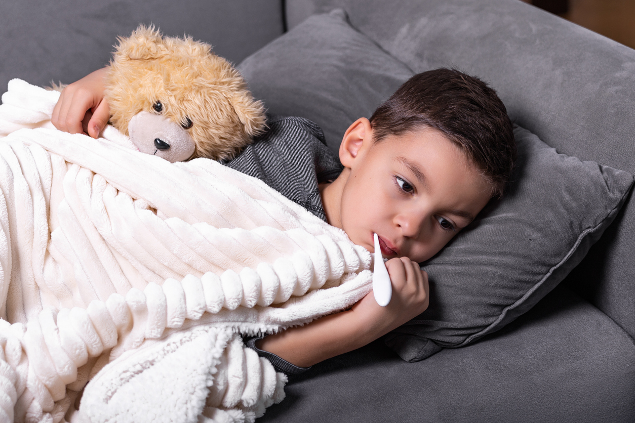 Sick boy with thermometer laying in bed. Sick child with fever and illness in bed. Flu. Cold