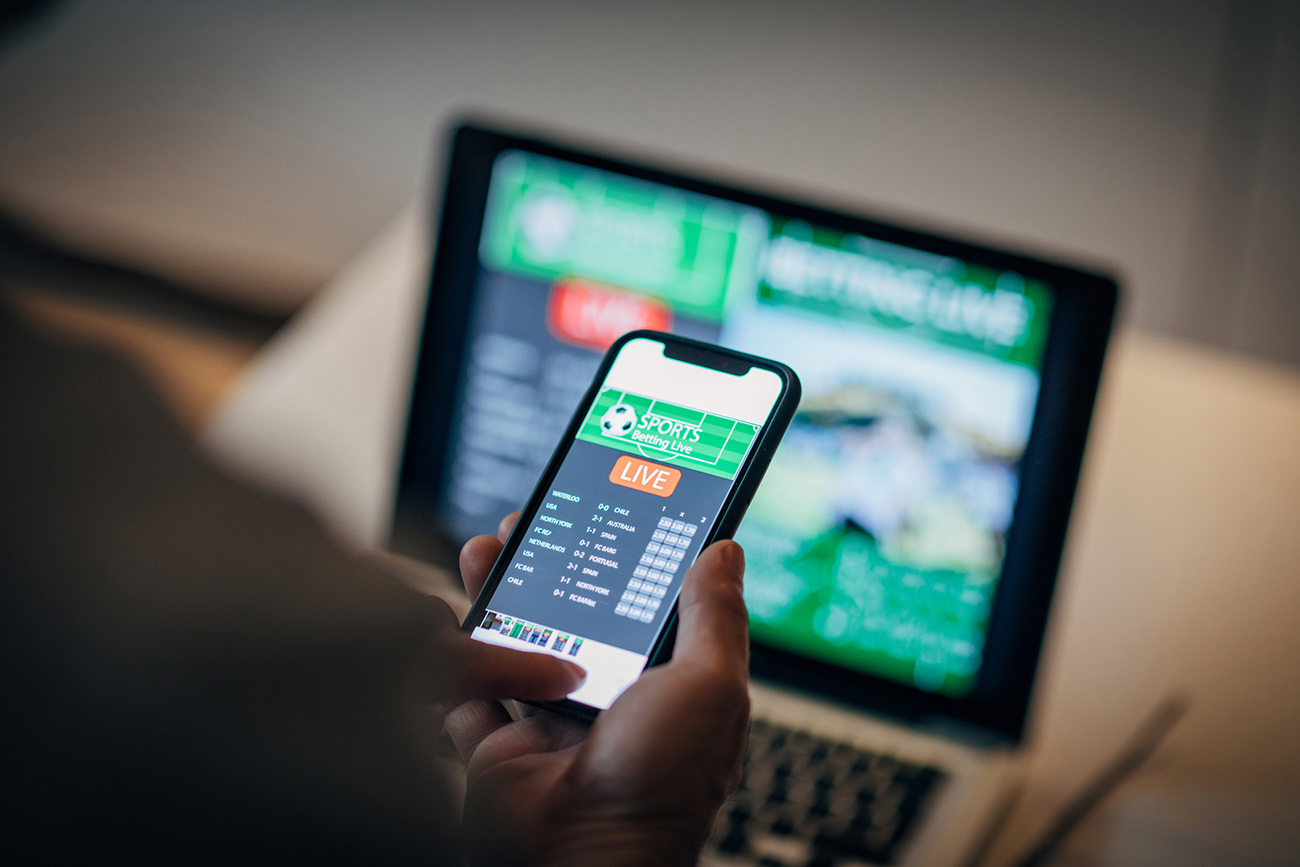 Mature man using mobile app for live betting and online gambling and watching a sports match
