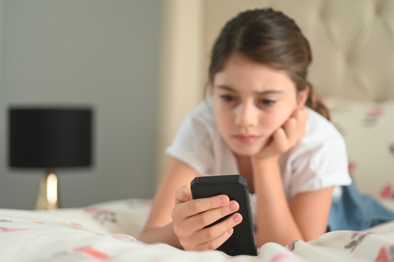 Sad girl (age 10) reading a bullying post on social media. Real people. Copy space