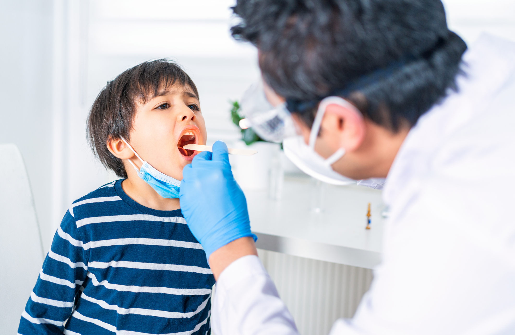 Male pediatrician examining little child patient’s throat at clinic