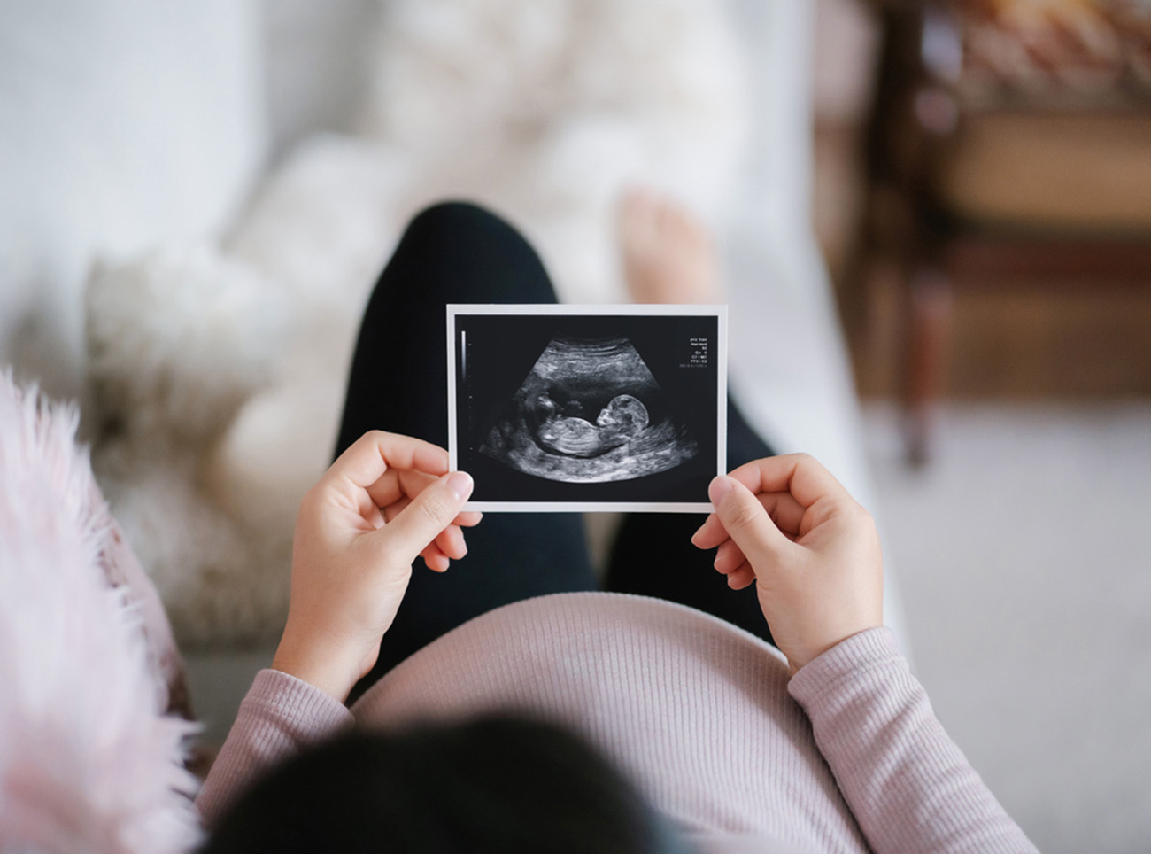 Young Asian pregnant woman lying on sofa at home, looking at the ultrasound scan photo of her baby. Mother-to-be. Expecting a new life concept