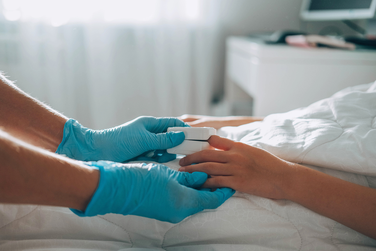 The child lies in bed, a doctor in medical gloves comes up to him and puts a pulse oximeter on his finger to measure the oxygen saturation. Asthma treatment.  Bedroom or hospital room for young patien