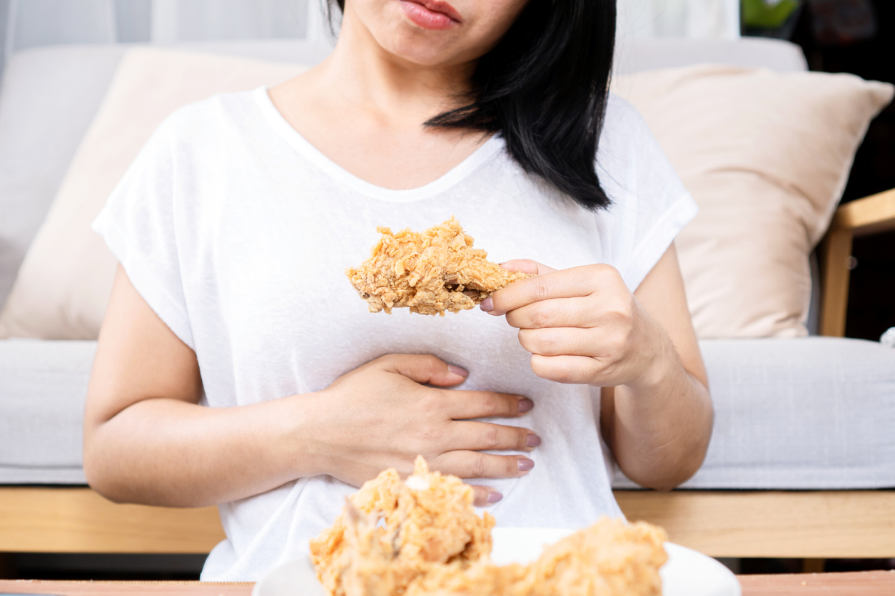 woman overeating fried chicken have a stomachache, indigestion because of eating too much, or binge eating disorder