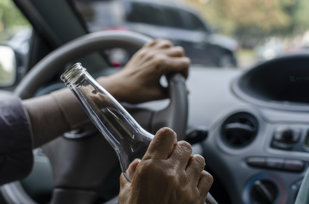 Drinking alcohol while driving. Drunk woman driving a car