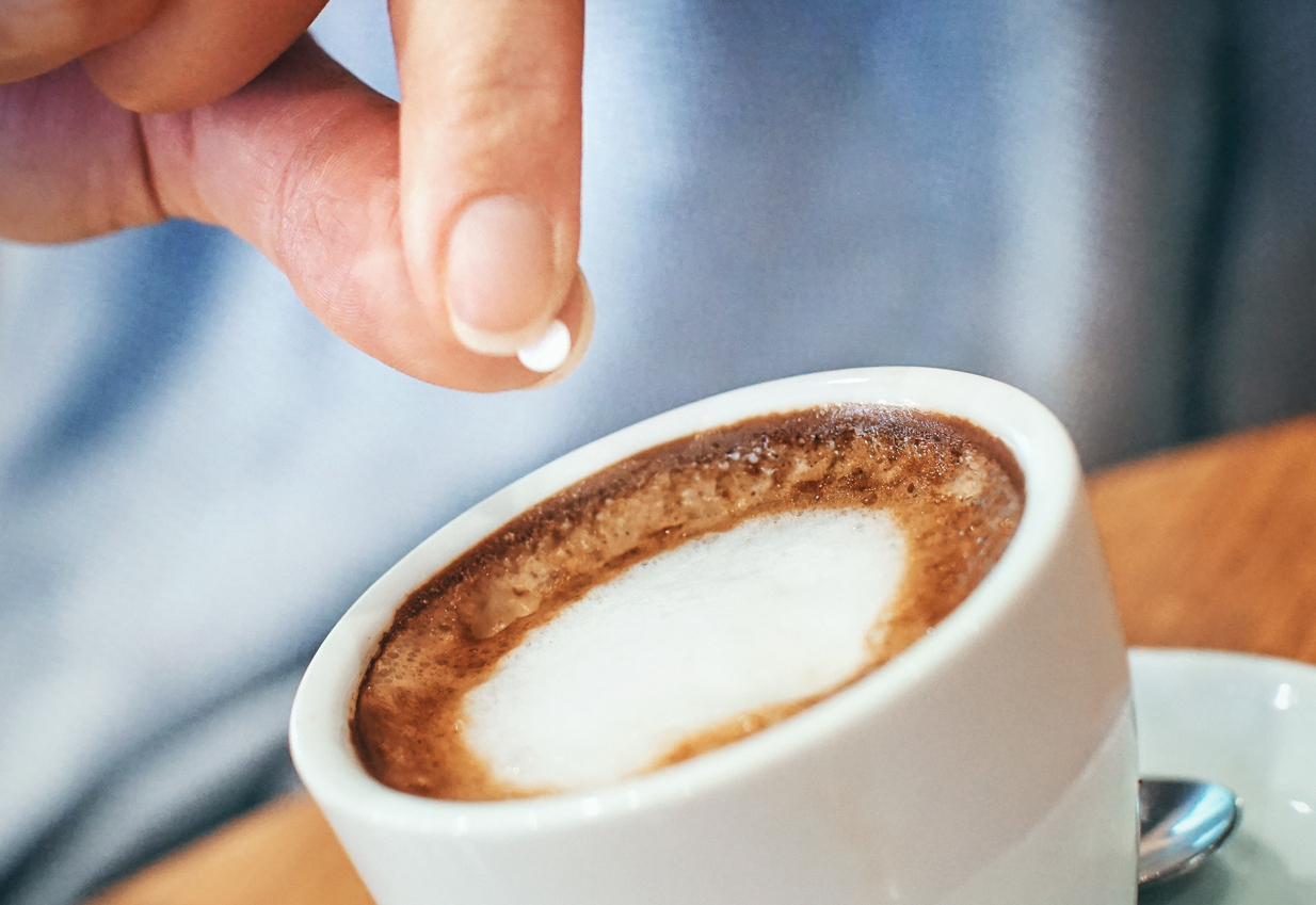 Closeup of unrecognizable woman putting one piece of artificial sweetener into her coffee. These sweeteners are based on aspartame or acesulfam compunds . Tilt shot.