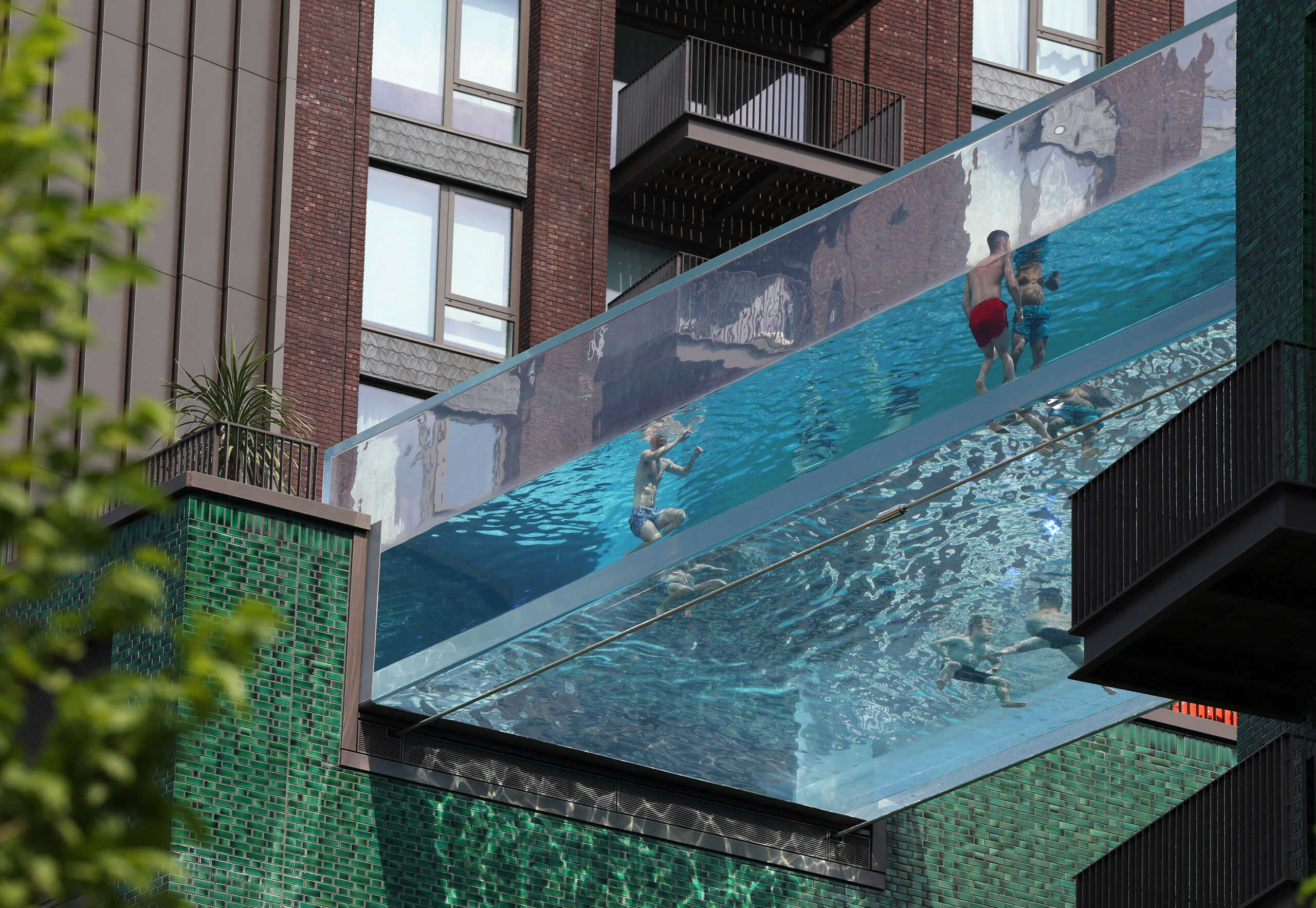People relax in a swimming pool suspended between two buildings as hot weather continues, in London, Britain, June 12, 2023. REUTERS