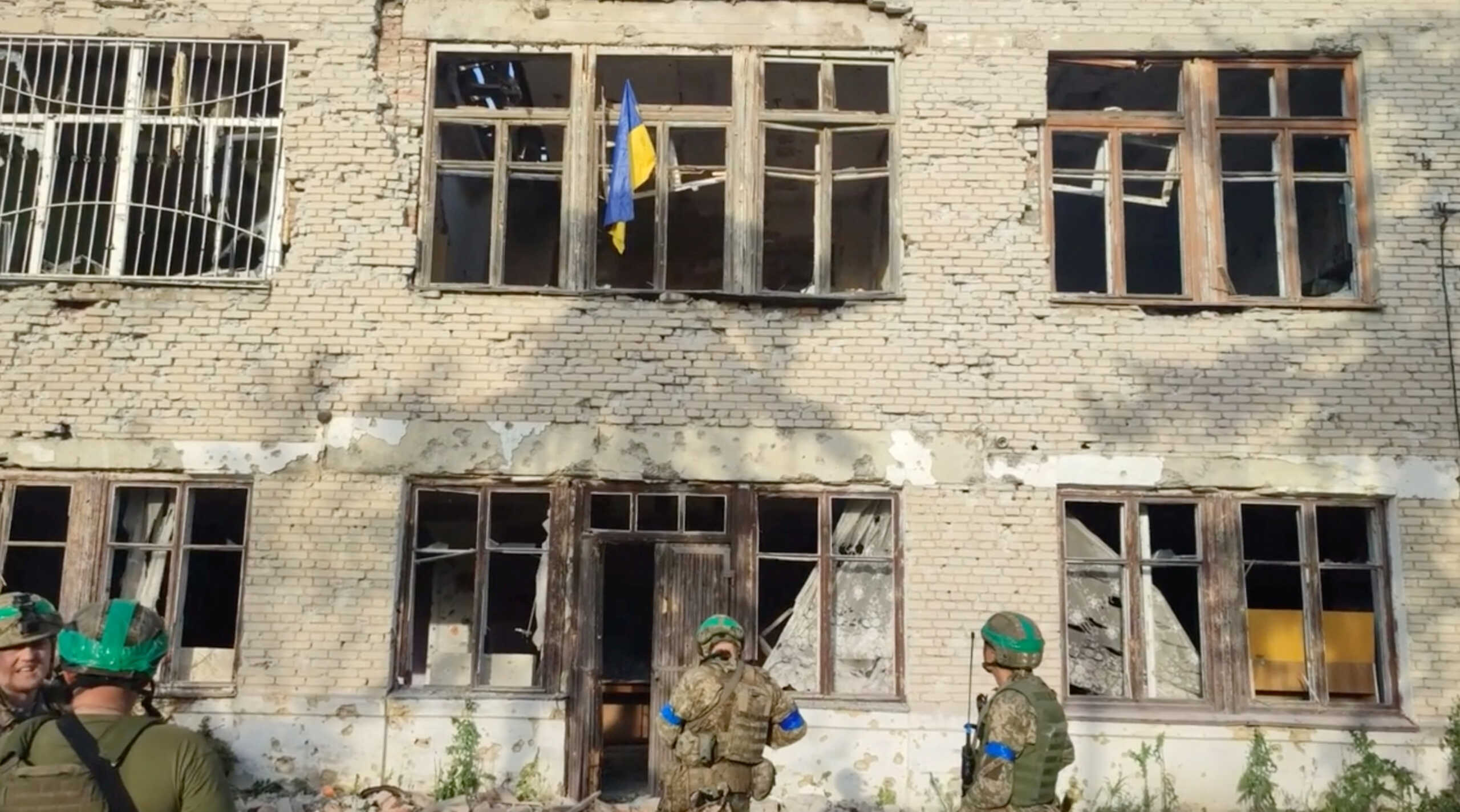 Ukrainian soldiers stand in front of a building with a Ukrainian flag on it, during an operation that claims to liberate the first village amid a counter-offensive, in a location given as Blahodatne, Donetsk Region, Ukraine, in this screengrab taken from a handout video released on June 11, 2023. 68th Separate Hunting Brigade 'Oleksy Dovbusha'