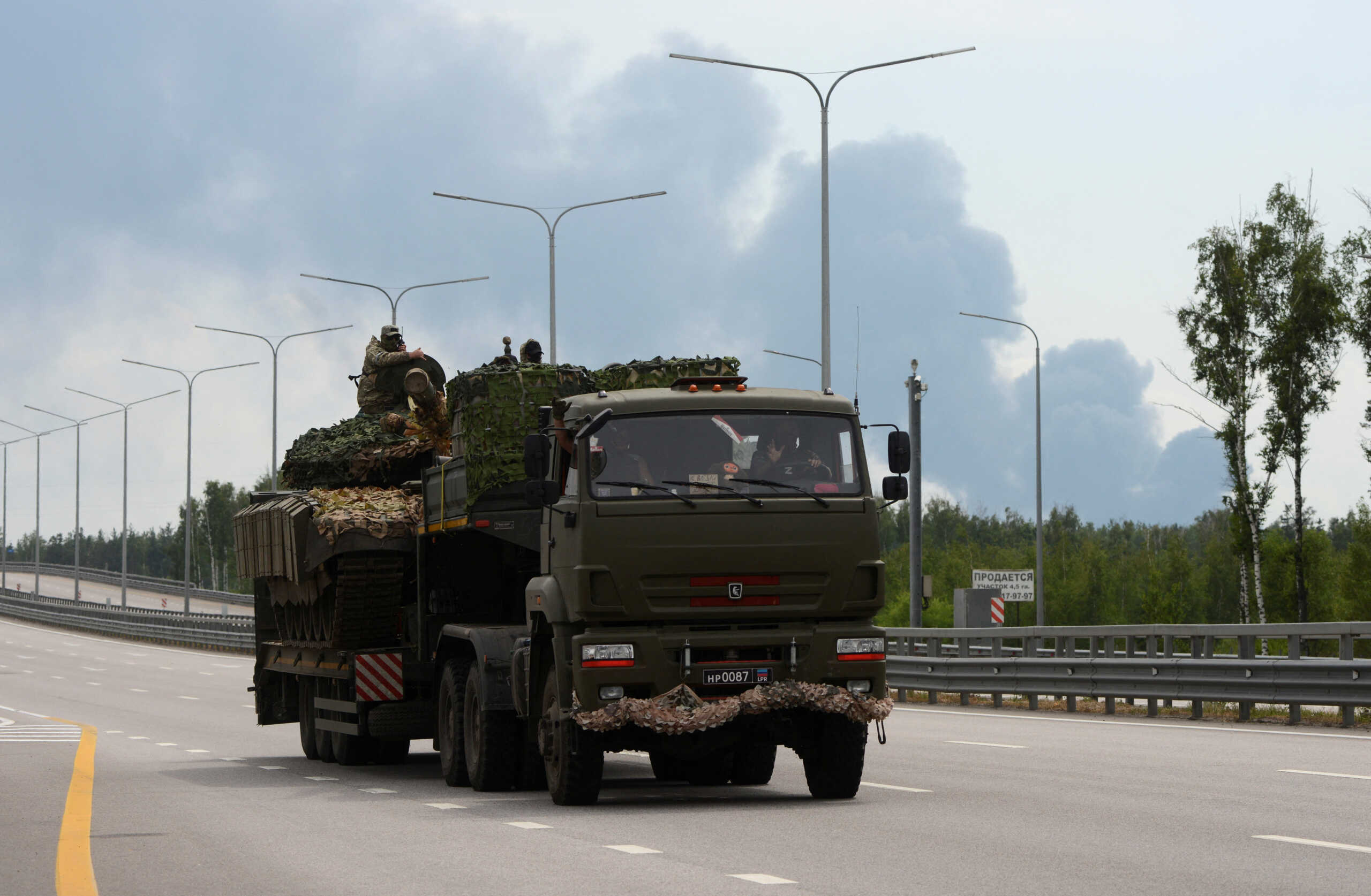 Fighters of Wagner private mercenary group transport a tank along M-4 highway, which links the capital Moscow with Russia's southern cities, with smoke from a burning oil depot seen in the background, near Voronezh, Russia, June 24, 2023. REUTERS