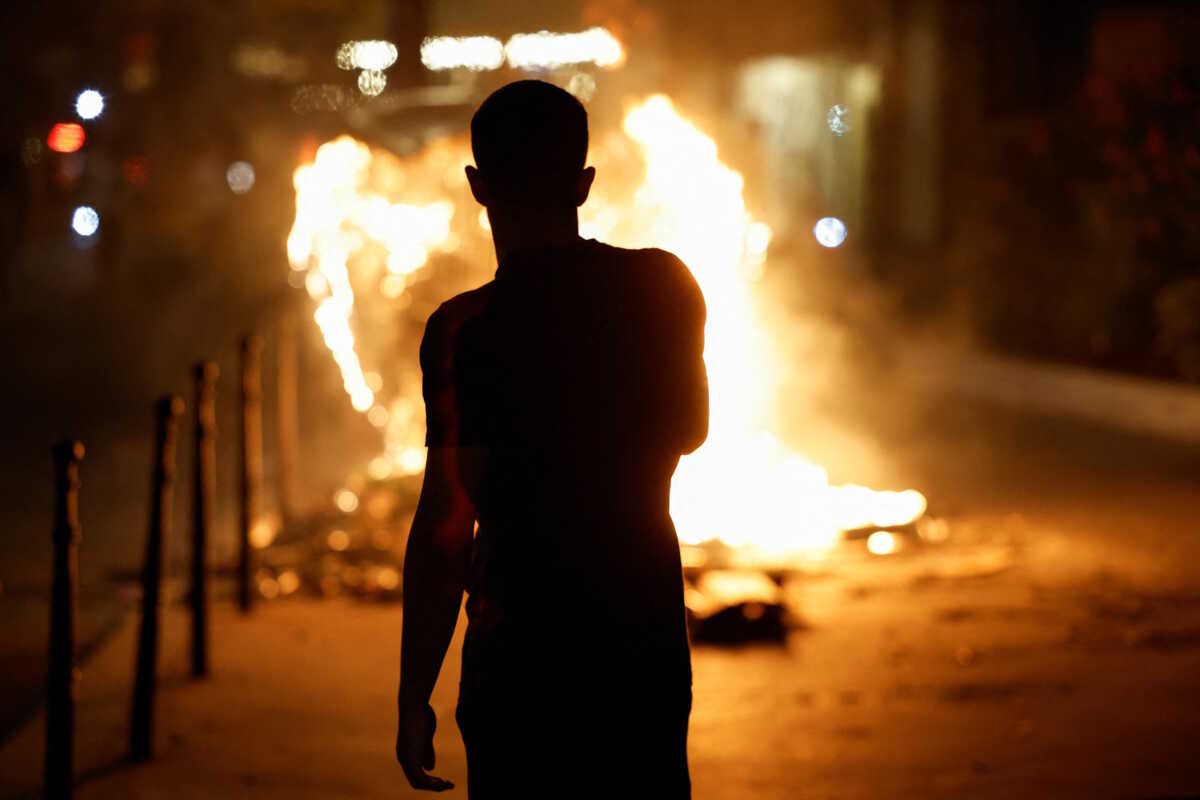 A person stands near a burning container as people protest following the death of Nahel, a 17-year-old teenager killed by a French police officer in Nanterre during a traffic stop, and against police violence, in Paris, France, June 30, 2023. REUTERS