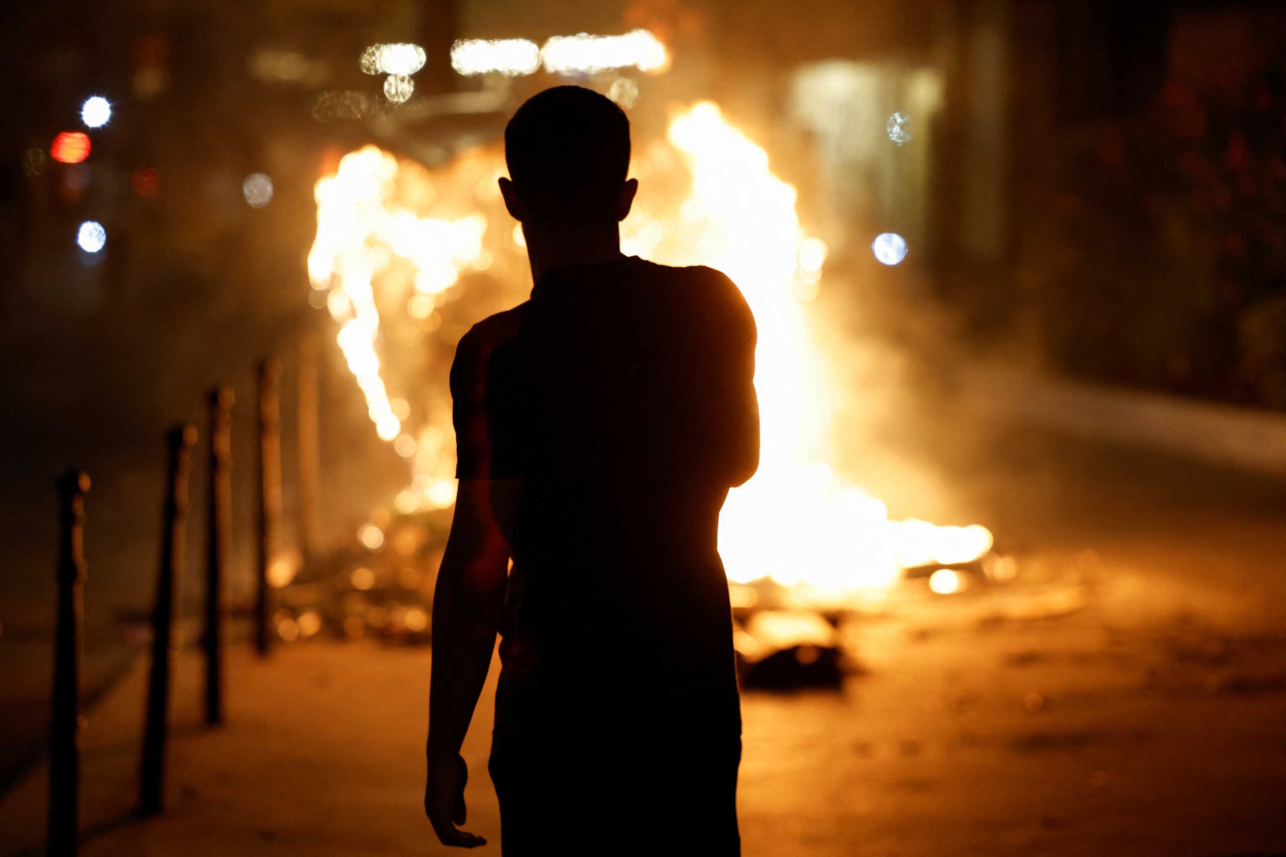 A person stands near a burning container as people protest following the death of Nahel, a 17-year-old teenager killed by a French police officer in Nanterre during a traffic stop, and against police violence, in Paris, France, June 30, 2023. REUTERS