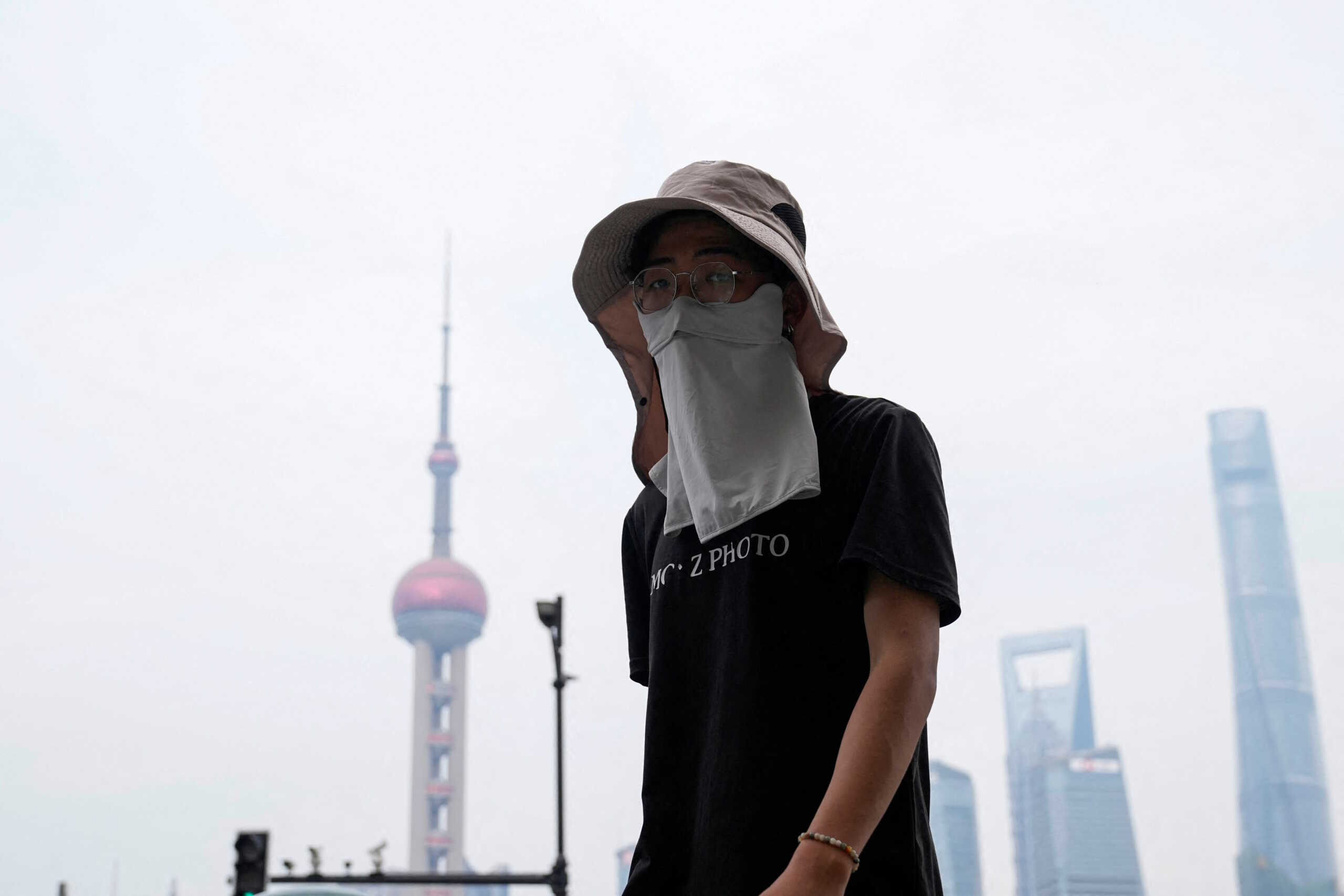 A man walks on the Bund as he shields himself from the sun with a hat and mask, on a hot day in Shanghai, China July 5, 2023. REUTERS