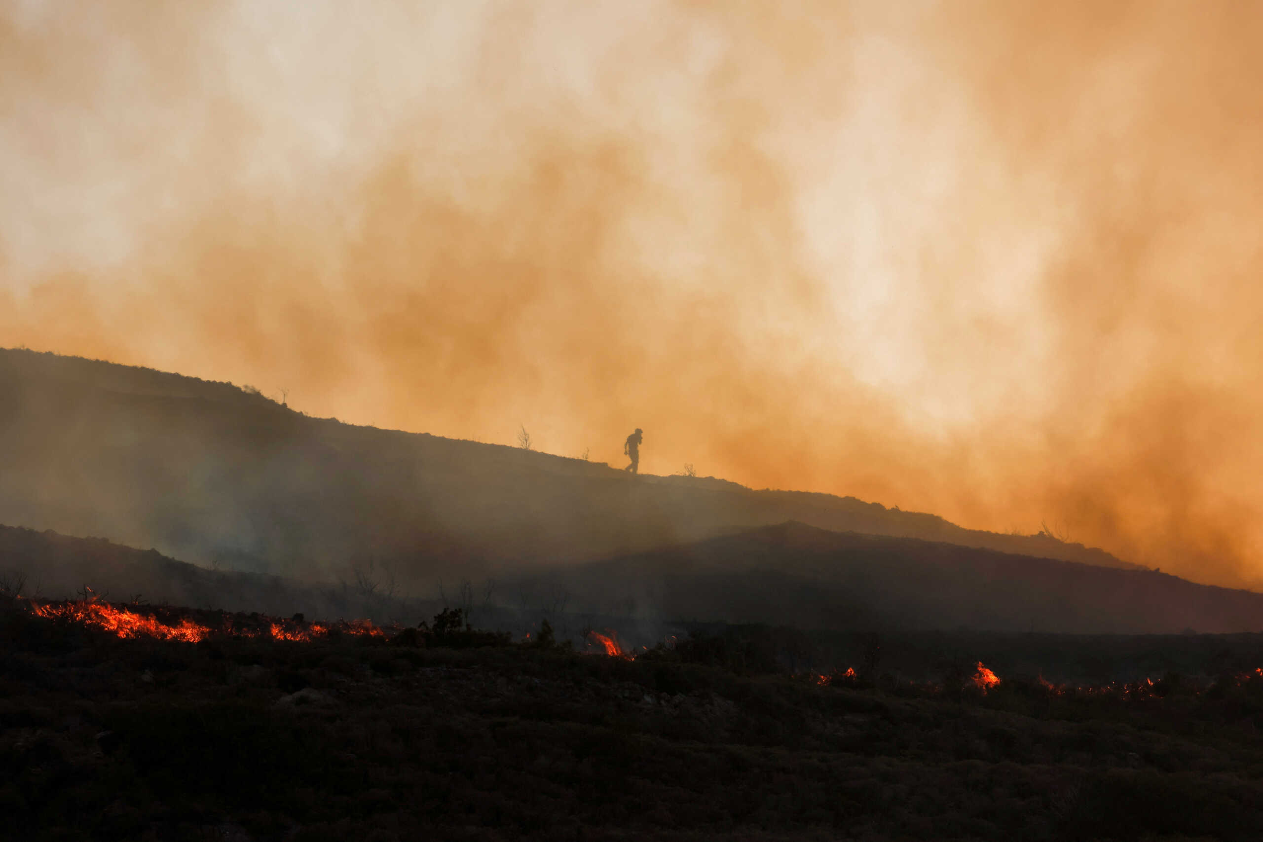 A man walks amid rising smoke as a wildfire burns in the village of Vati, on the island of Rhodes, Greece, July 26, 2023. REUTERS