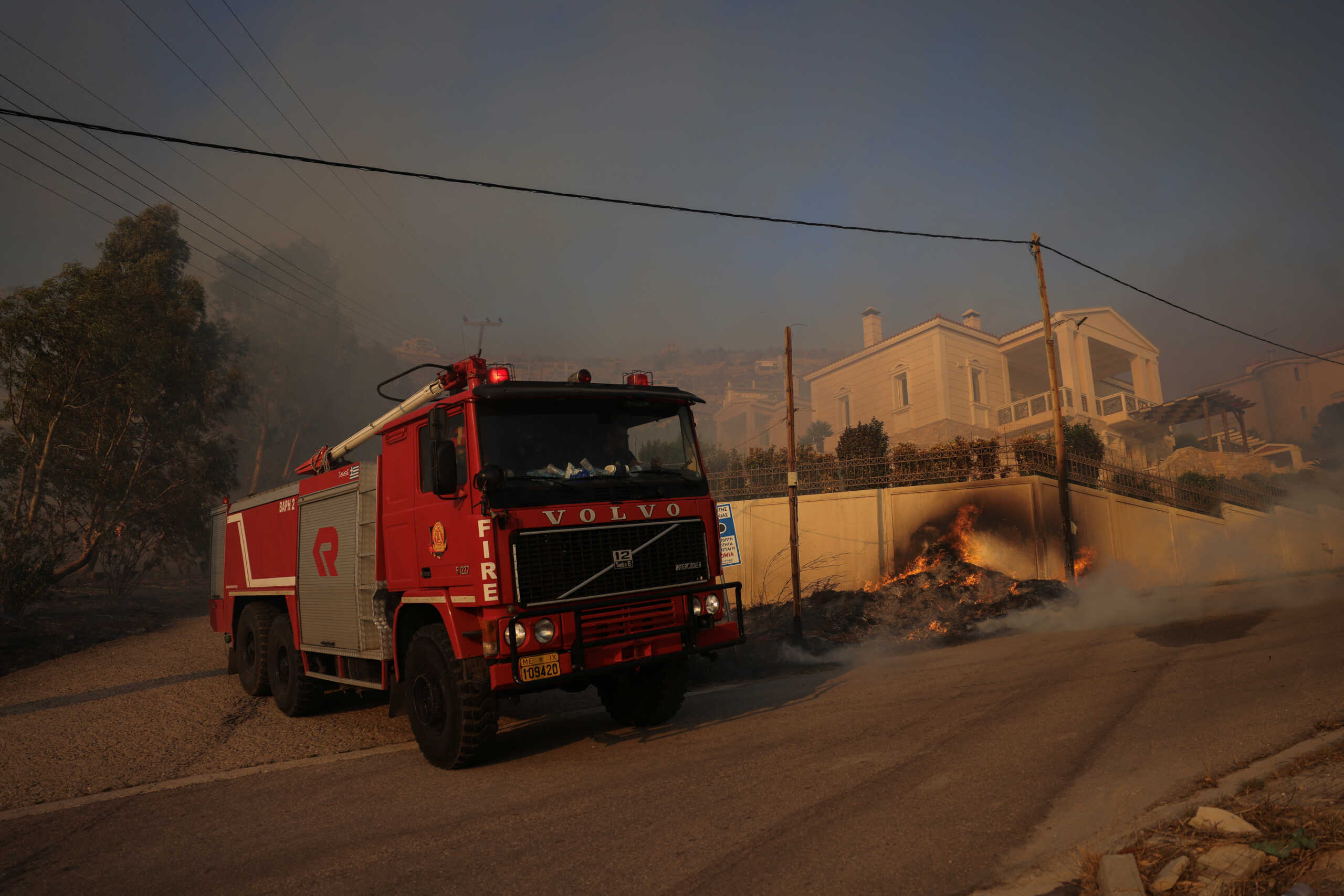 A firefighting truck is parked next to a house, as a wildfire burns in Saronida, near Athens, Greece, July 17, 2023. REUTERS