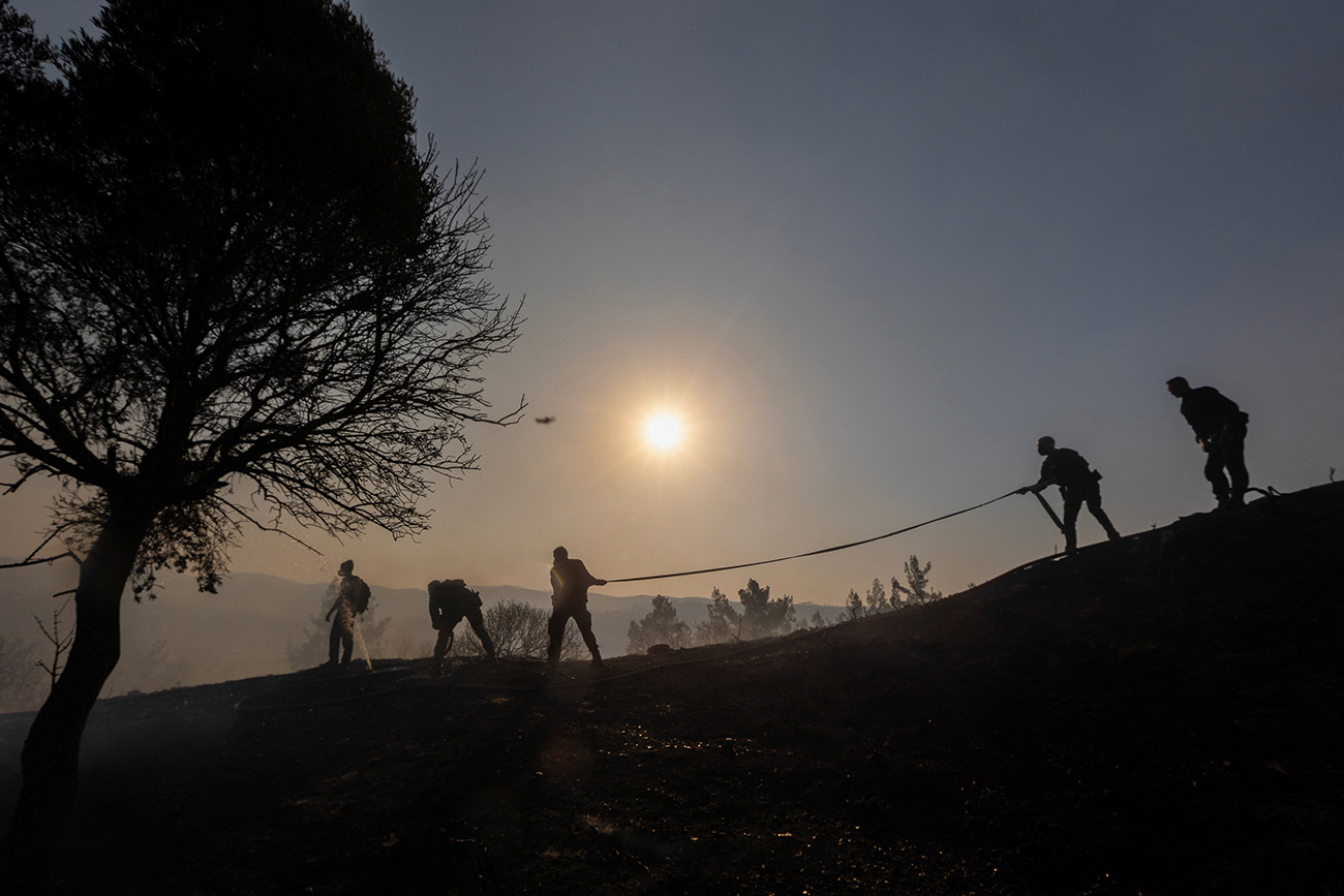 Firefighters, volunteers and police officers are silhouetted while carrying a hose, as a wildfire burns near the village of Asklipieio, on the island of Rhodes, Greece, July 24, 2023. REUTERS
