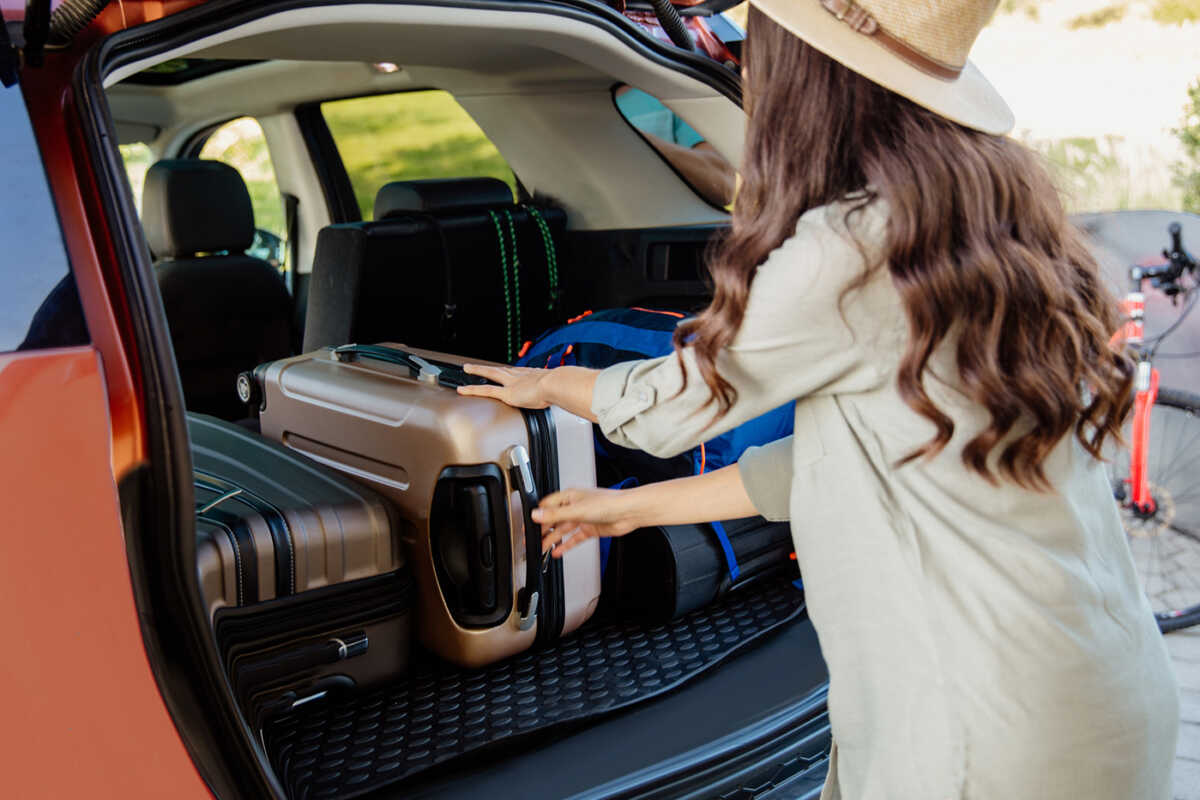 Rear view of a woman holding bag standing near car boot
