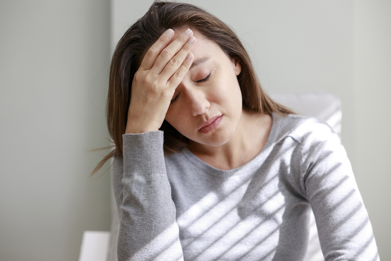 Shot of a young woman holding her head in discomfort due to pain at home