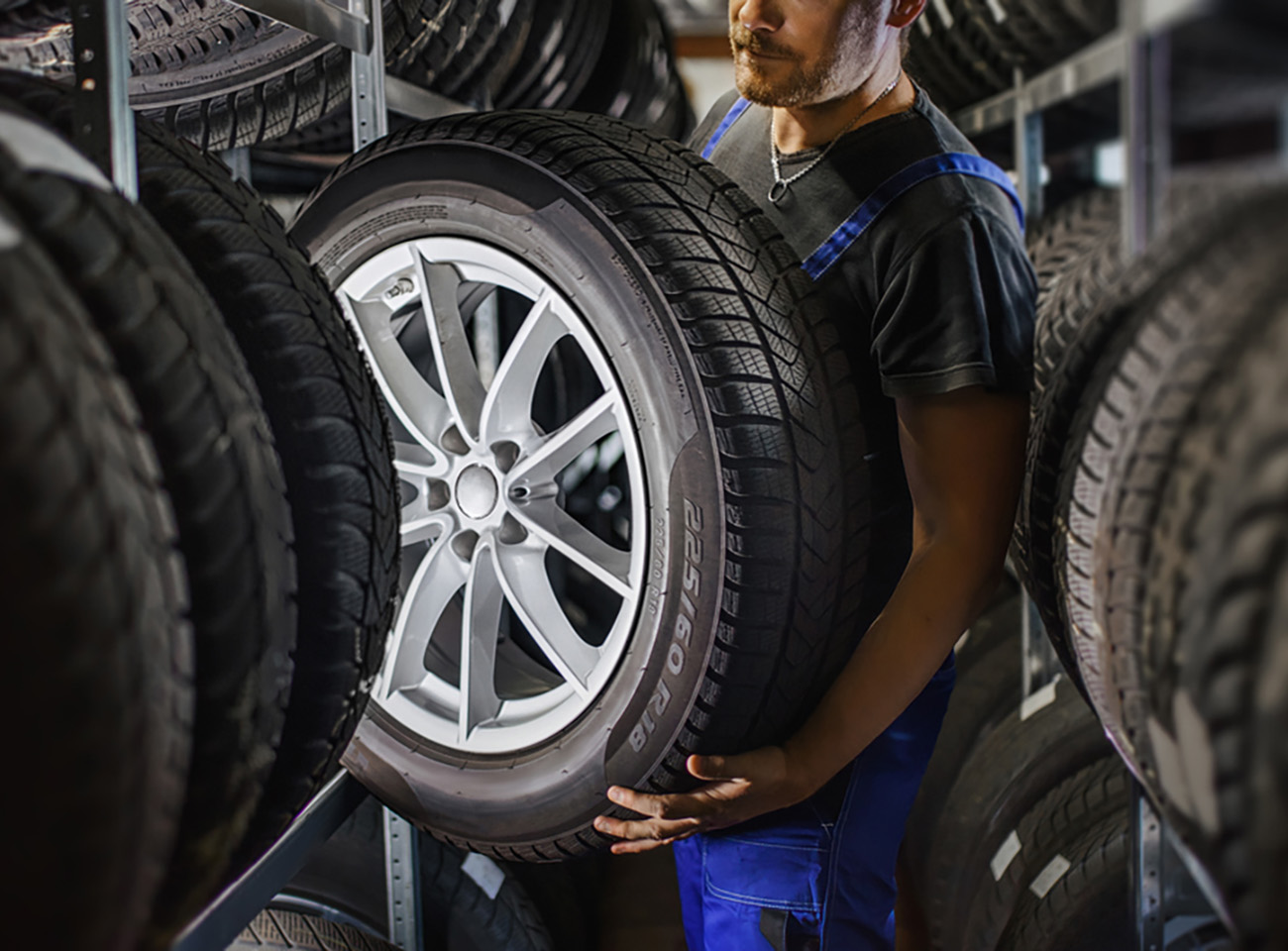 Hardworking experienced worker holding tire and he wants to change it In the tire store. Selective focus on tire.