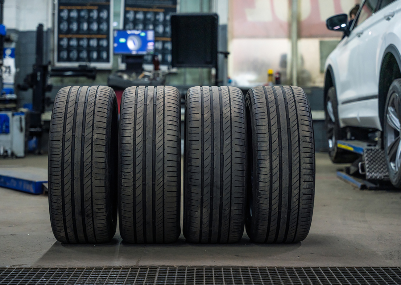 Set of used and dirty summer tires at tire service and car on a lift