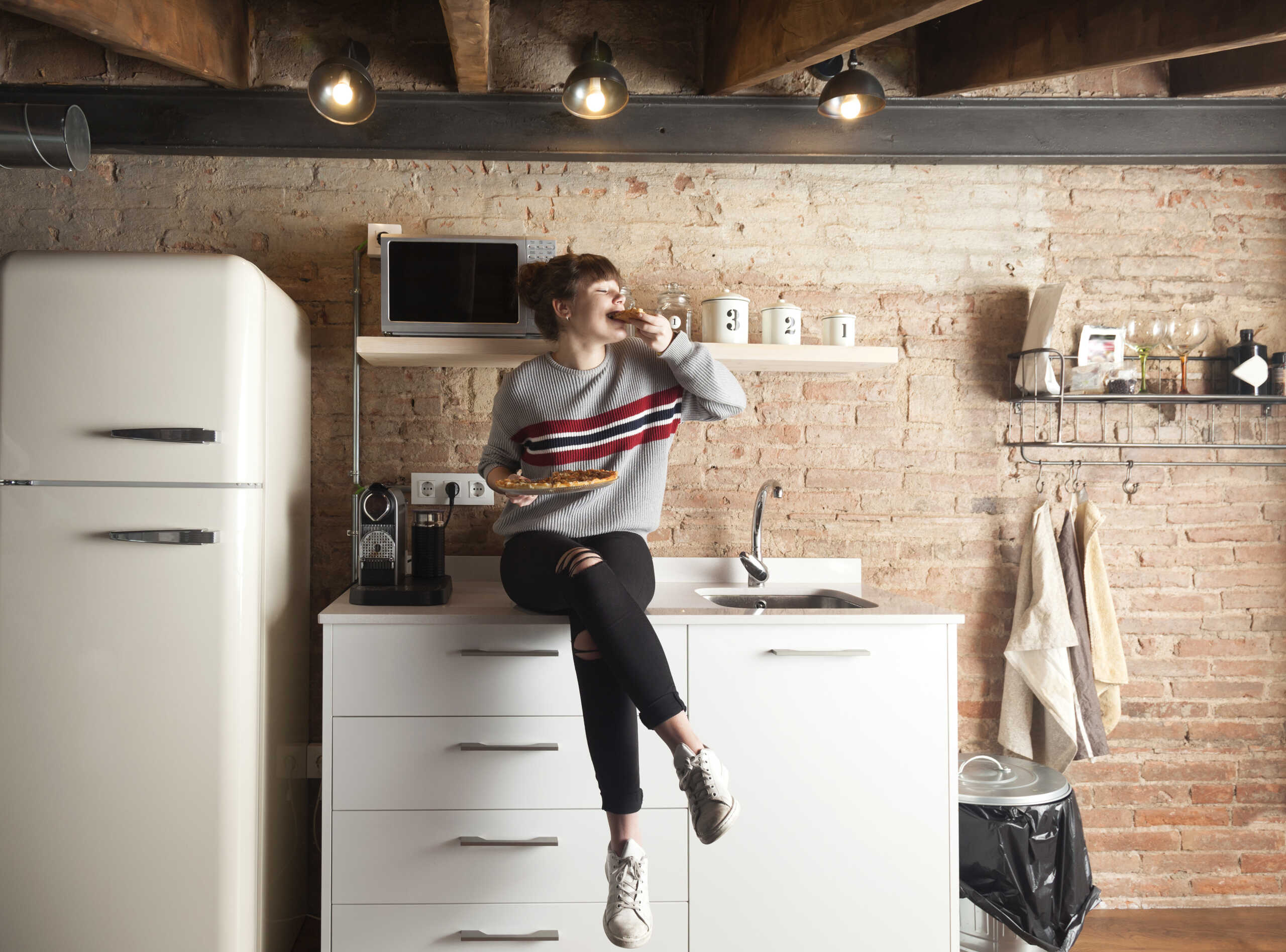 Beautiful girl eating pizza in a modern kitchen