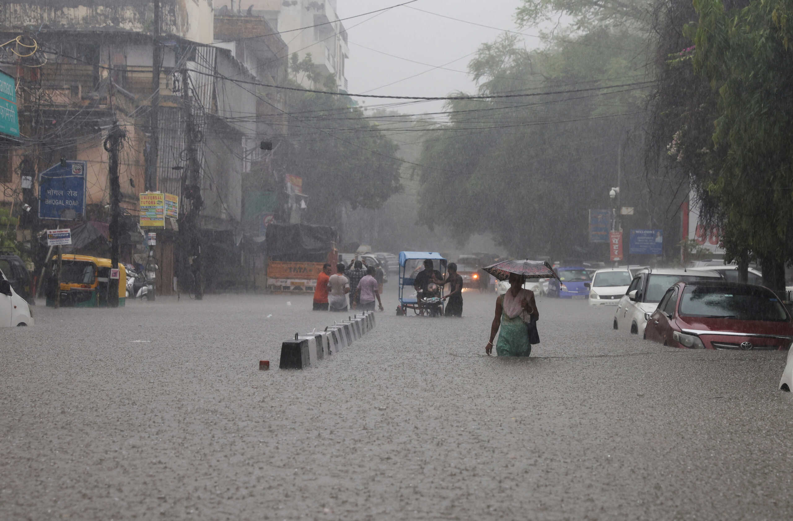 People wade through a flooded street after heavy rains in New Delhi, India, July 8, 2023. REUTERS