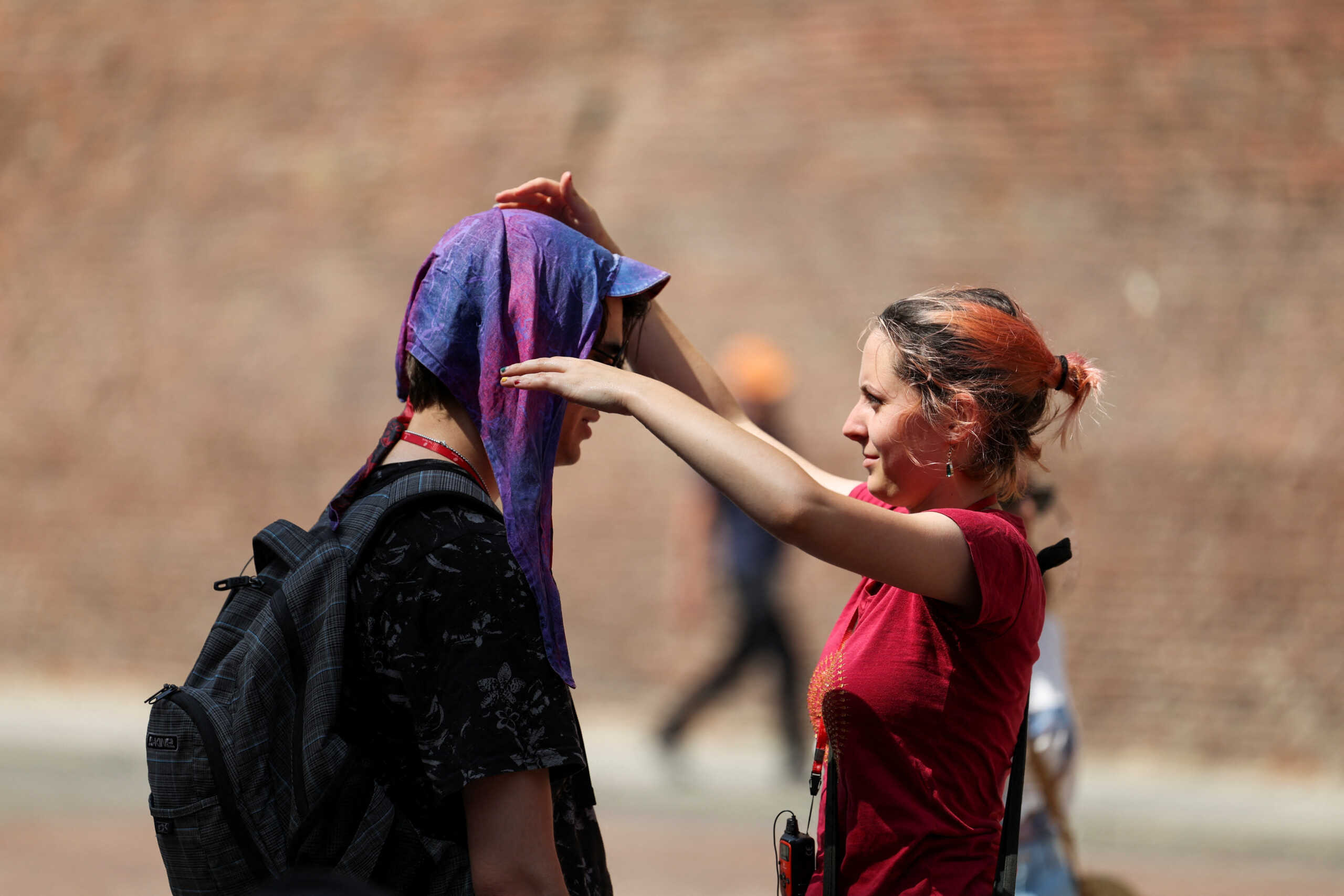 A woman puts wet head scarf to protect a man from the sun, during a heatwave across Italy as temperatures are expected to rise further in the coming days, in Bologna, Italy July 18, 2023. REUTERS