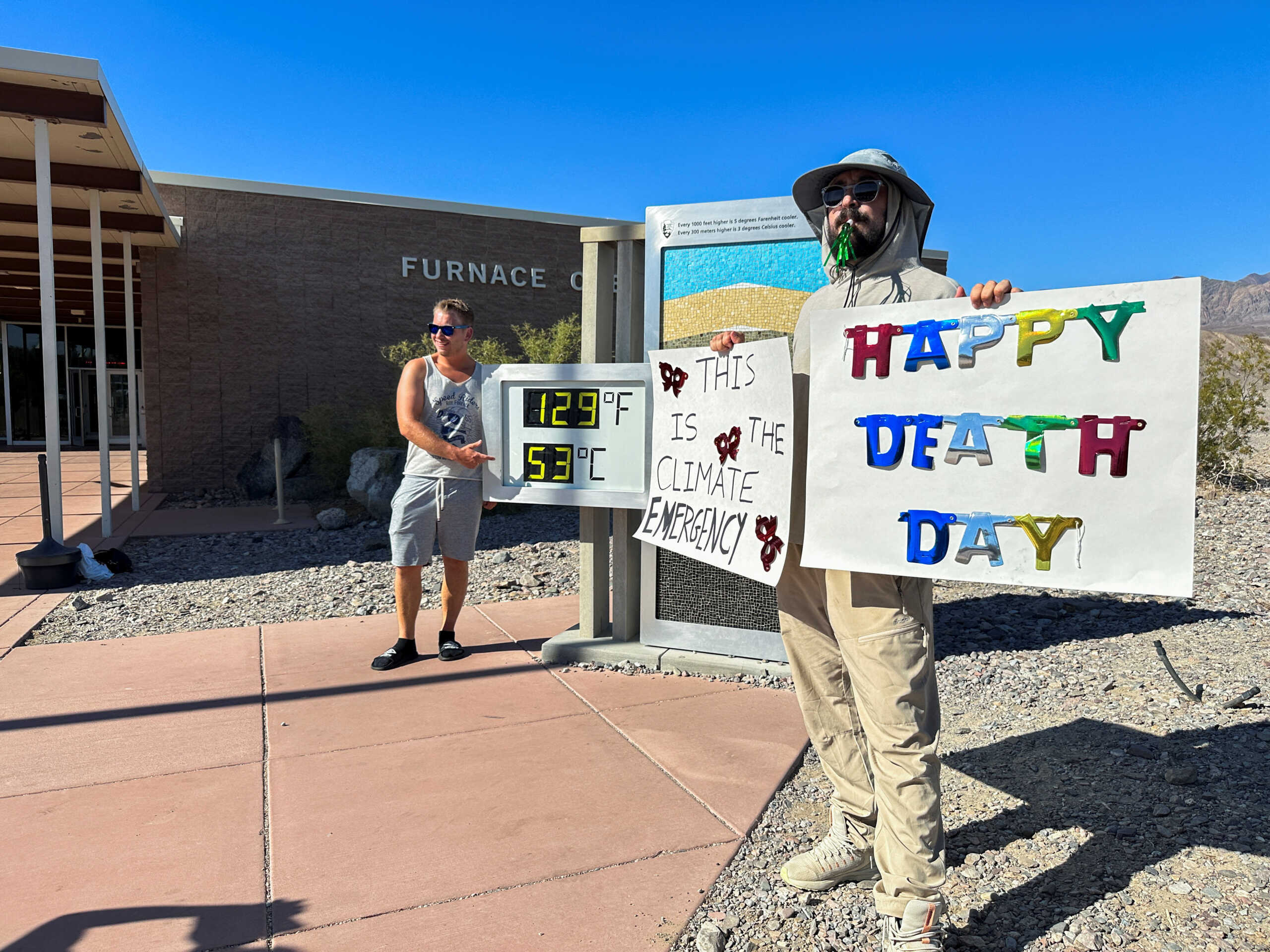 A man holds placards in front of a digital sign displaying the high temperature, in Death Valley, California, U.S. July 15, 2023. REUTERS