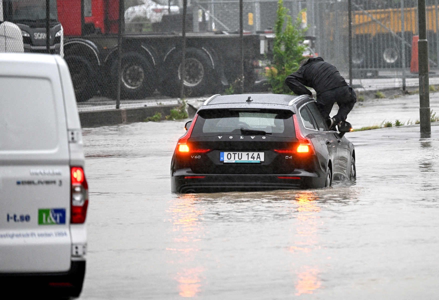 A man climbs out of a car that tried to get through a flooded roundabout in Arlov on the closed flooded E6 outside Malmo, Sweden August 7, 2023. TT News Agency