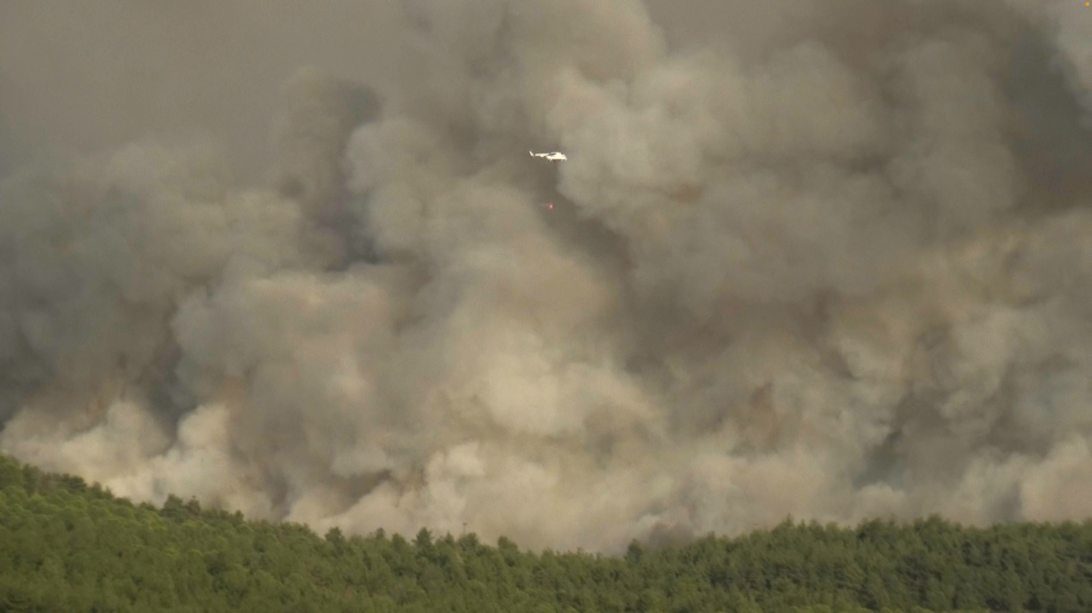 A helicopter carries a water bucket as a wildfire burns in Canakkale, Turkey, August 22, 2023, in this screen grab obtained from a social media video. Gurkan Duzenli