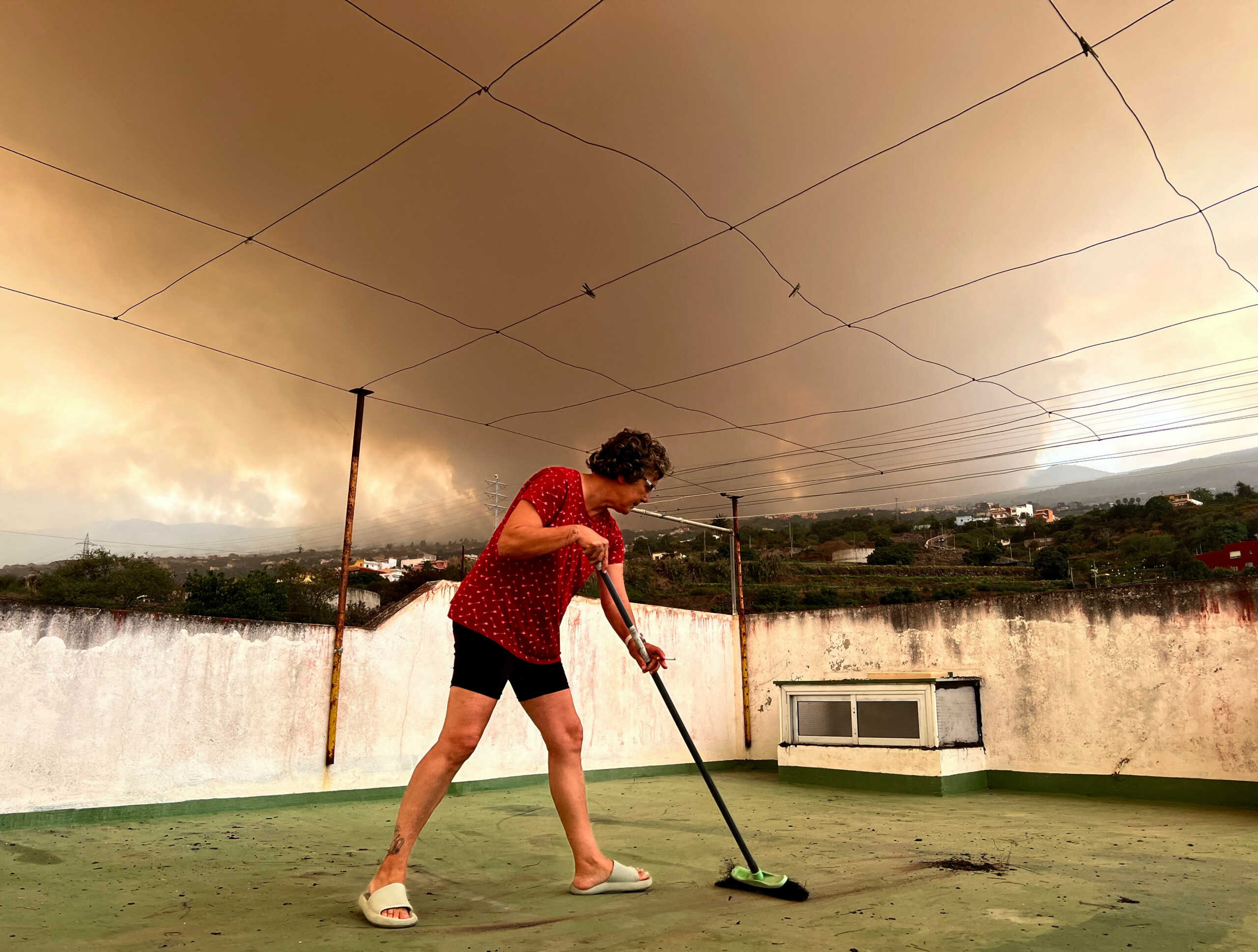 Josefina Minguillon, 62, sweeps the ash off the terrace of her house while smoke rises over the village of Benijos, as wildfires rage out of control on the island of Tenerife, Canary Islands, Spain August 19, 2023. REUTERS