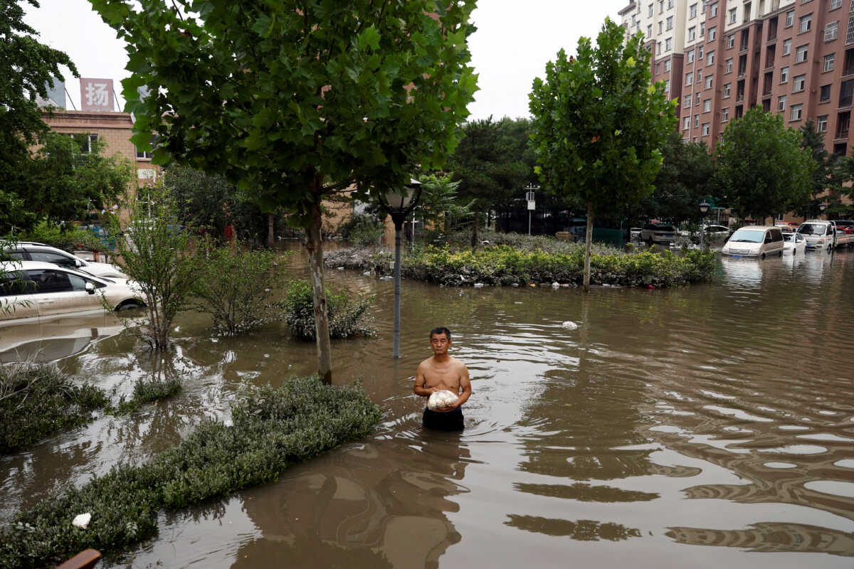 FILE PHOTO: A man holding a bag of food wades through floodwaters after the rains and floods brought by remnants of Typhoon Doksuri, in Zhuozhou, Hebei province, China August 3, 2023. REUTERS
