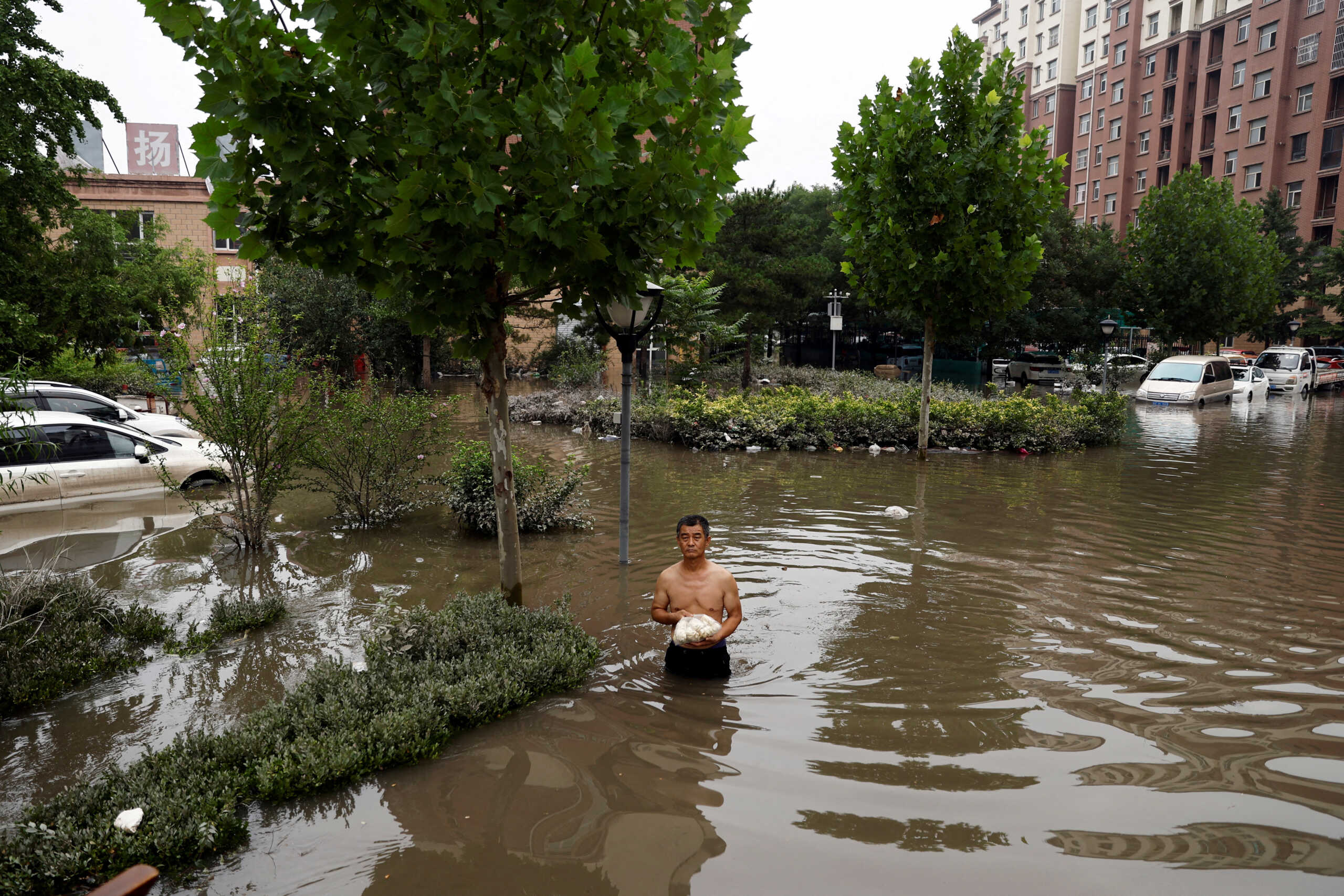 FILE PHOTO: A man holding a bag of food wades through floodwaters after the rains and floods brought by remnants of Typhoon Doksuri, in Zhuozhou, Hebei province, China August 3, 2023. REUTERS