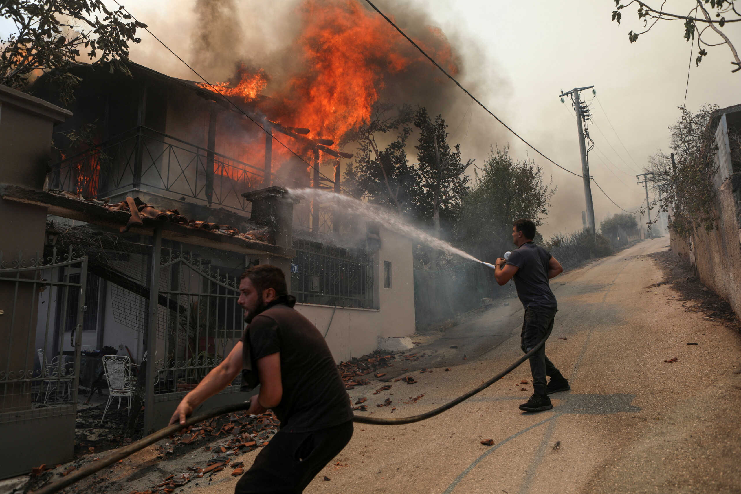 Volunteers try to extinguish a fire burning a house, as a wildfire burns in Menidi, near Athens, Greece, August 23, 2023. REUTERS