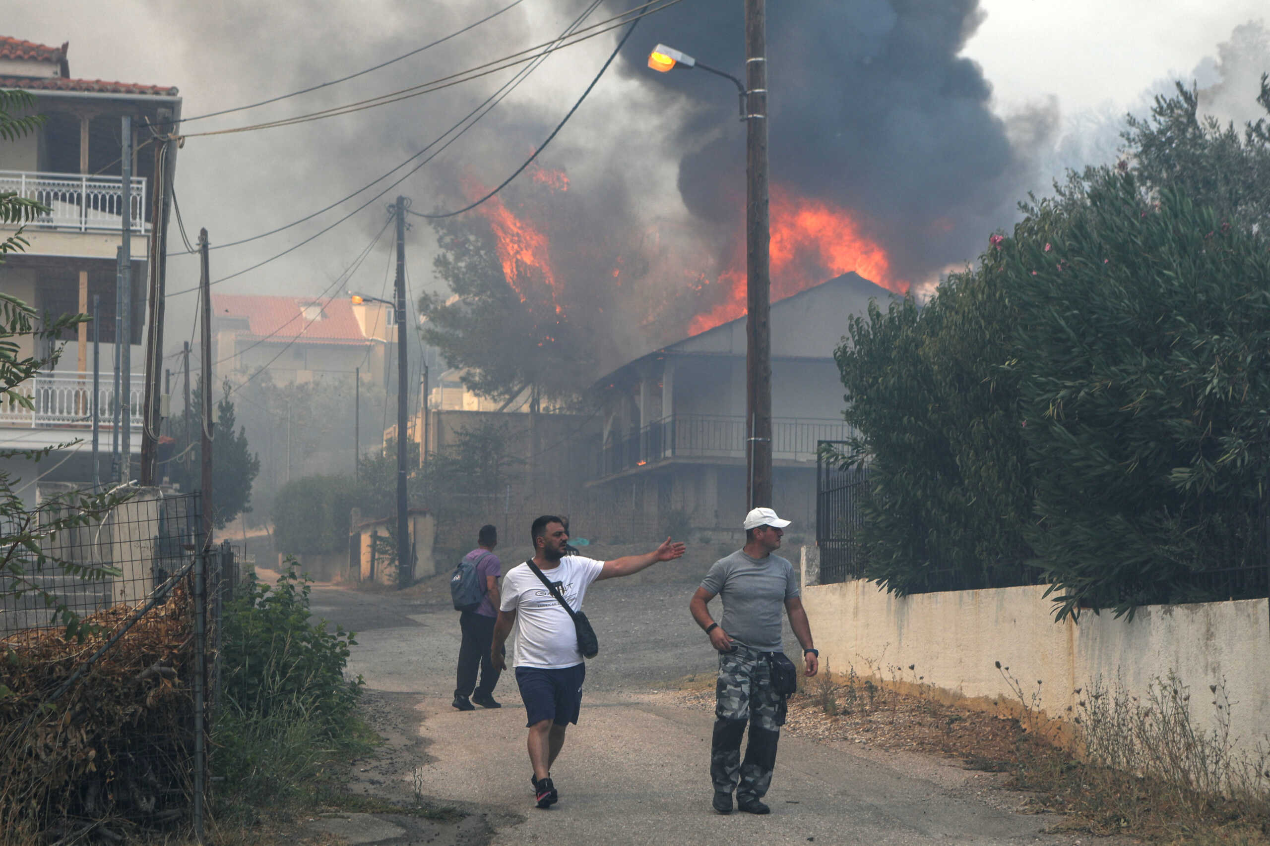 Local residents walk near a burning house, as a wildfire rages in Menidi, near Athens, Greece, August 23, 2023. REUTERS