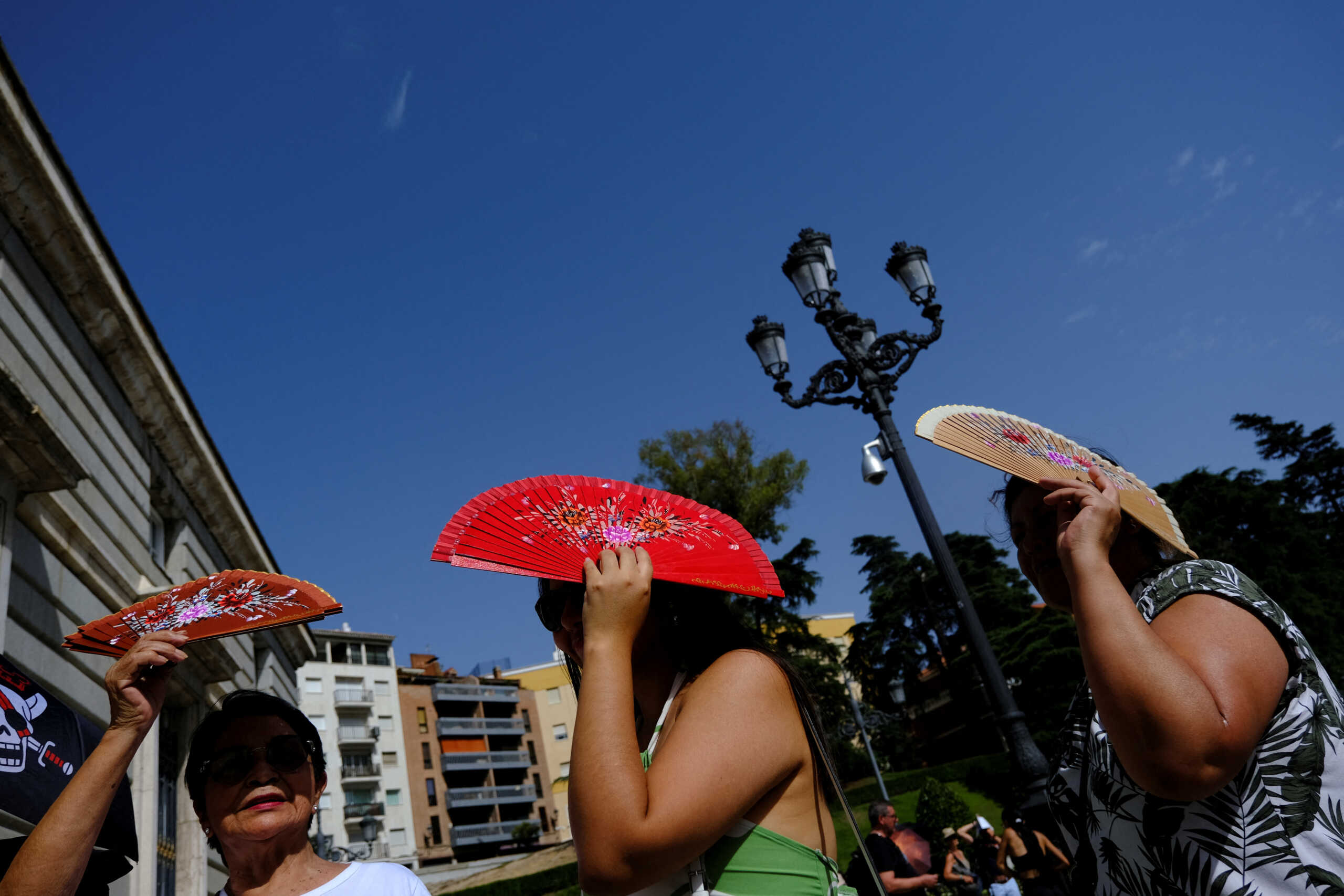 Peruvian nationals Sadith Ushinagui, 74, Alisson Carrillo, 29, and Carol Ore, 50, protect themselves from the sun with fans as they wait to enter the Royal Palace during the third heatwave of the summer in Madrid, Spain, August 8, 2023. REUTERS