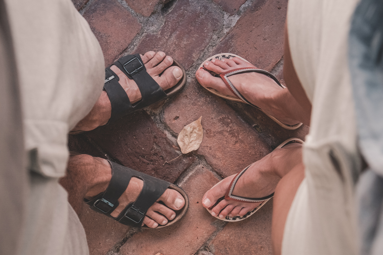 Top down view of man and woman wearing sandals and flip flops facing eachother. Summertime, adventure, backpacking, traveling concept