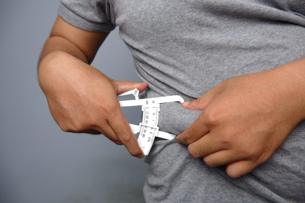 asian man wearing grey shirt checking his fat belly with calipers