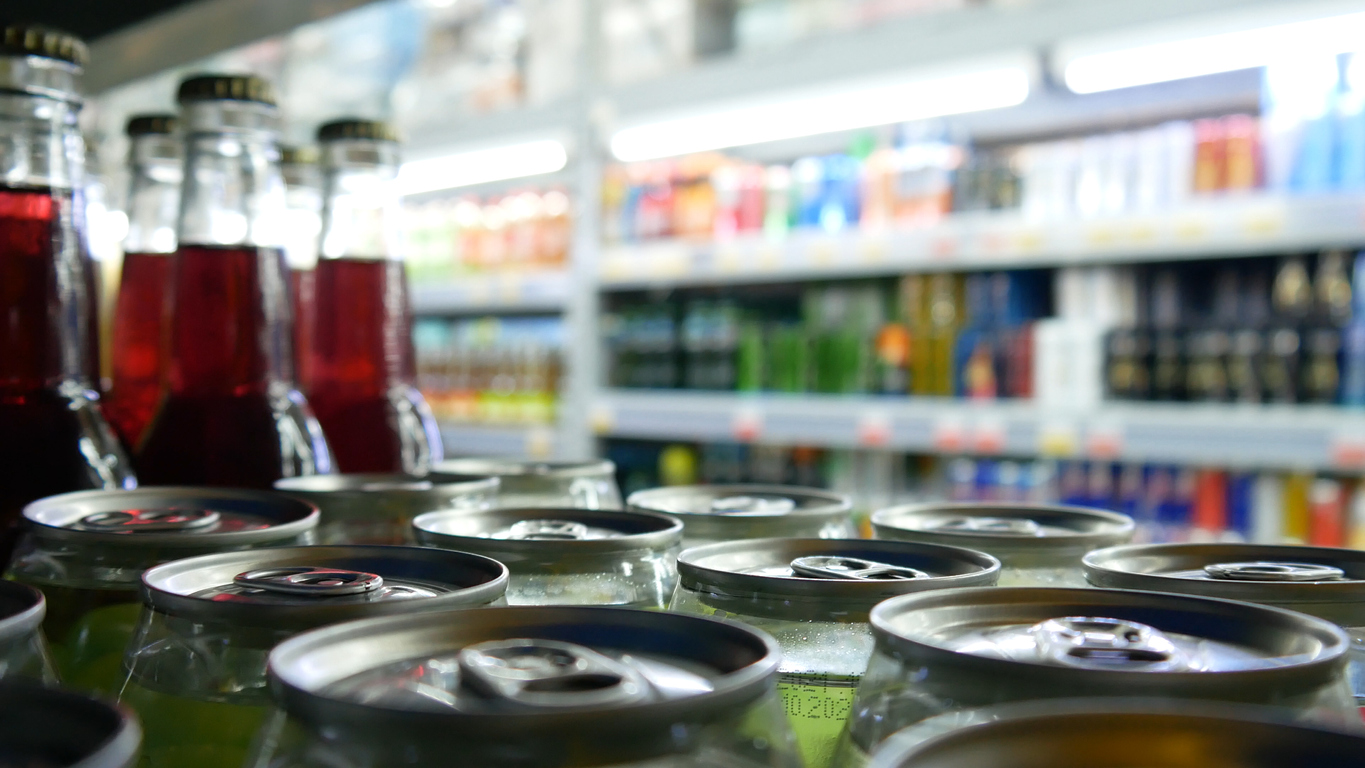 Many colorful cans and bottles of soda on store shelves close-up