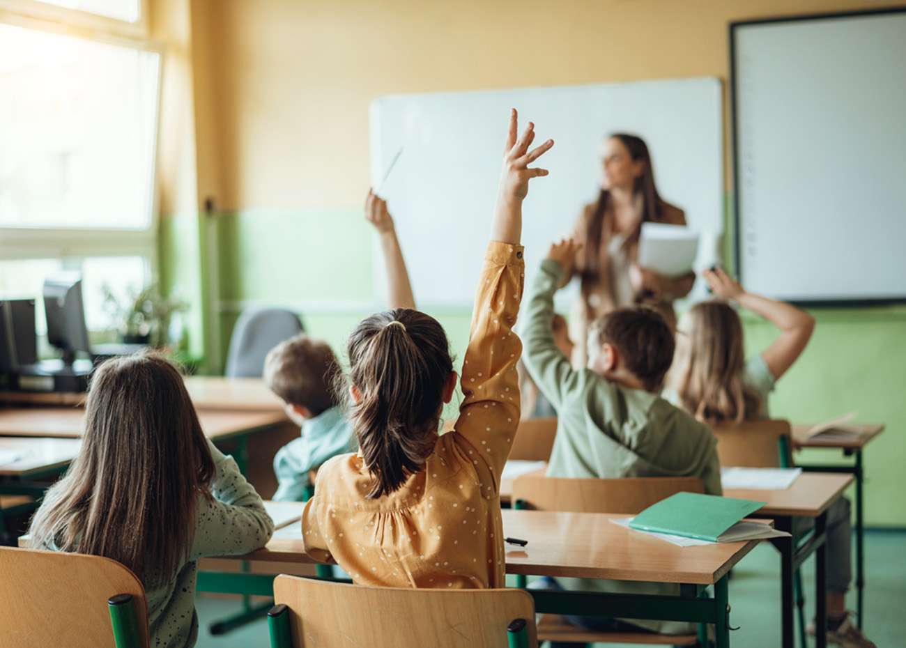 Students raising hands while teacher asking them questions in classroom
