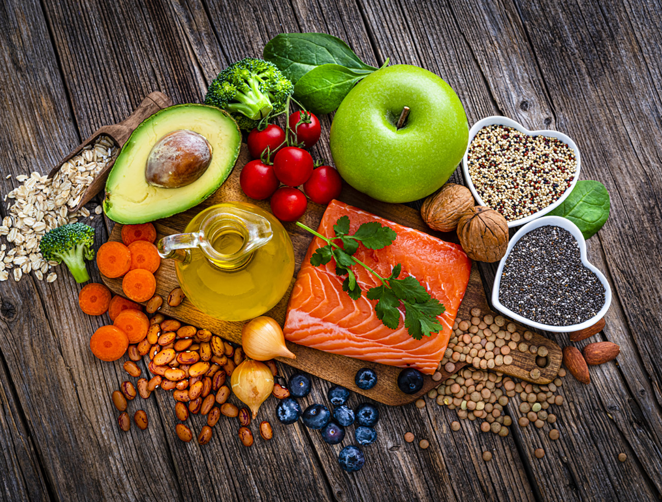 Overhead view of a group of food for heart care and lower cholesterol shot on rustic wooden table. The composition includes salmon, olive oil, chia seeds, quinoa, broccoli, avocado, green apple, oatmeal, spinach, brown lwntil, pinto bean, onion, almonds, walnut, carrot blueberries among others. High resolution 42Mp studio digital capture taken with SONY A7rII and Zeiss Batis 40mm F2.0 CF lens