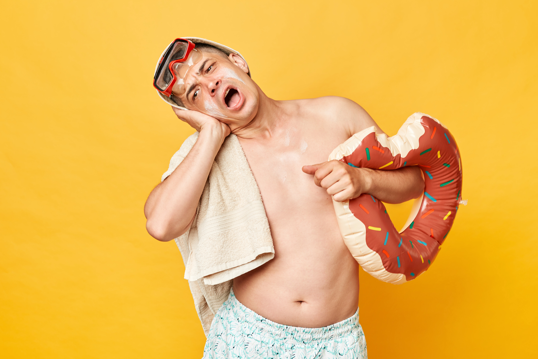 Despair sick adult man wearing shorts swimsuit snorkeling goggles holding donut rubber ring and bag isolated on yellow background feeling strong pain in his ear screaming.