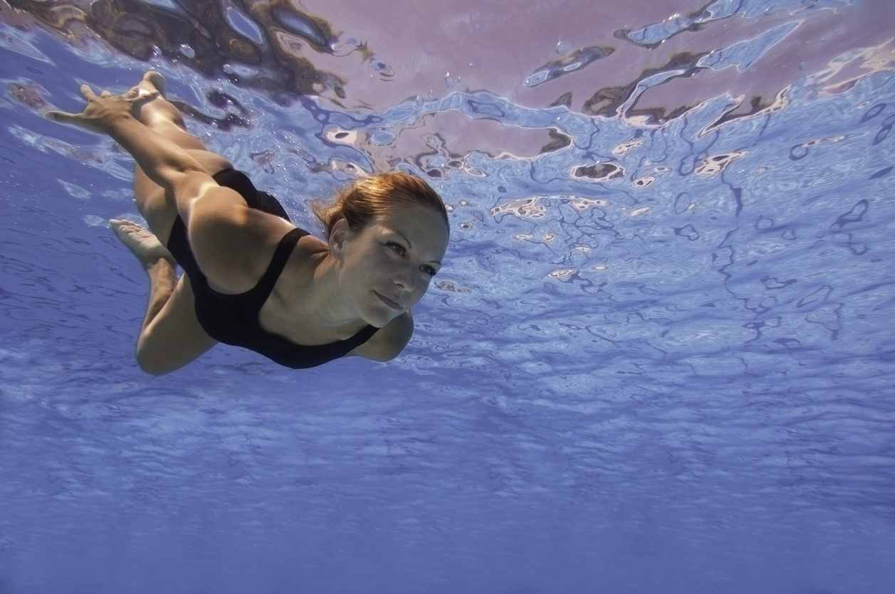 "Attractive female swimming under the water surface with eyes opened. Focused on face, polarizing filter, convenient copy space"