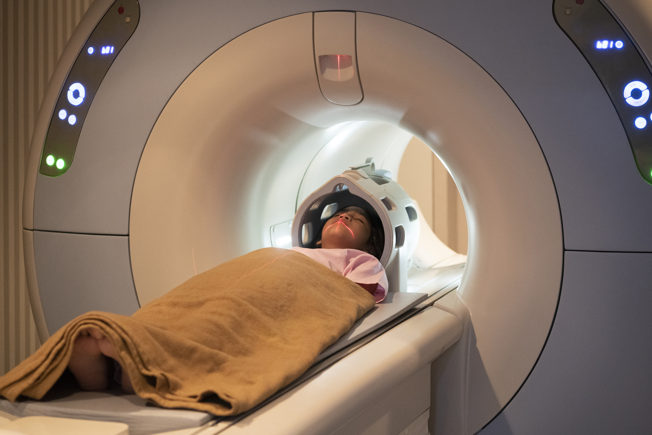 Young female patient laying straight, with blanket over her, inside tube of MRI scanner