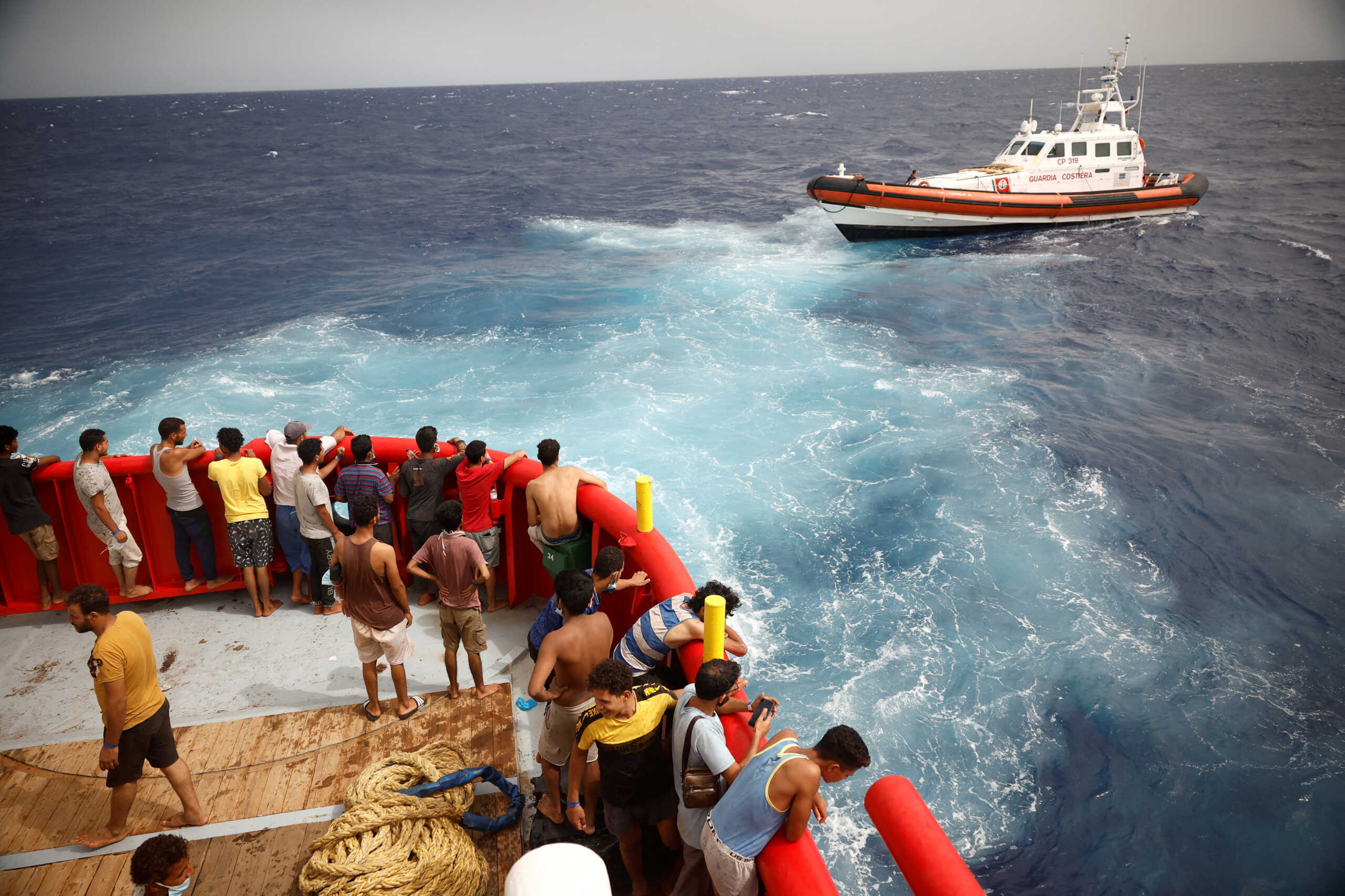 FILE PHOTO: Migrants on board of NGO Proactiva Open Arms Uno rescue boat looks at boat Guardia Costiera heading to Lampedusa island, in central Mediterranean Sea, close to Lampedusa island, Italy, August 19, 2022. REUTERS